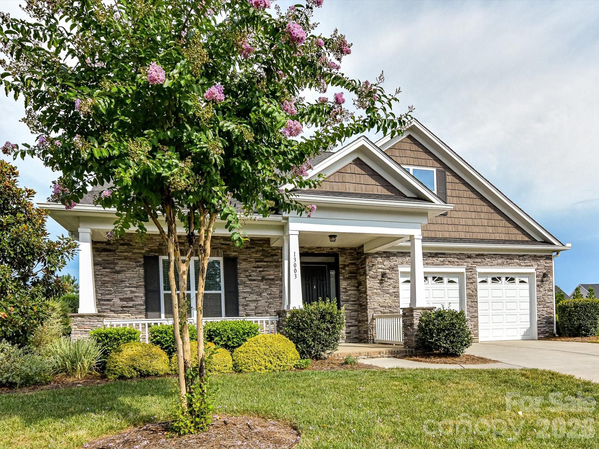 Beautifully maintained home offers charming curb appeal with stone accents, a welcoming covered front porch, manicured landscaping, and a two-car garage. - 13003 Riley Grace Lane, Cornelius