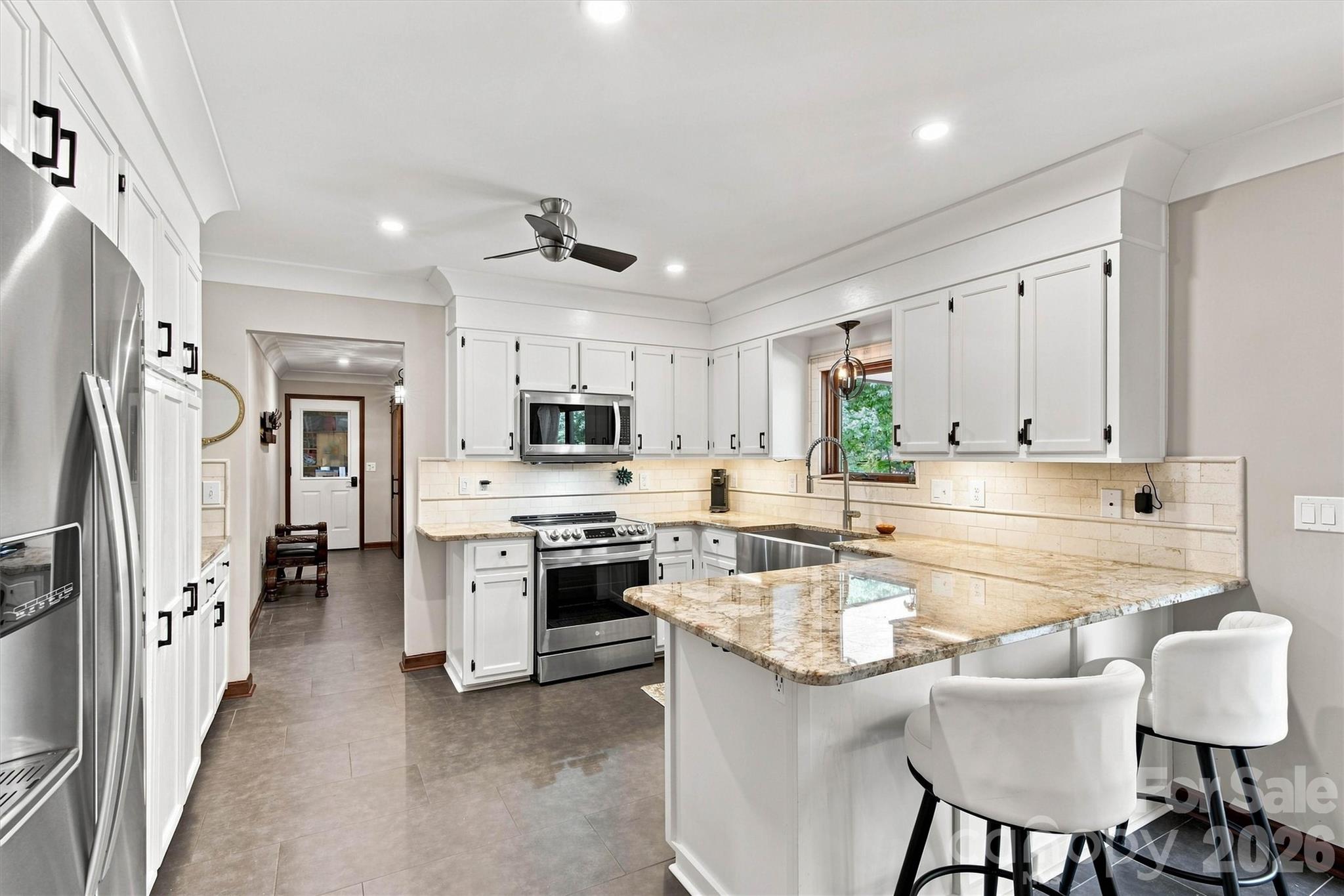 Beautifully renovated kitchen featuring tile flooring, granite countertops, tile backsplash, and updated lighting. Includes a stainless steel farmhouse sink, stainless steel appliances (including refrigerator), and updated cabinetry with under-cabinet lighting. - 3867 Angie Drive, Denver
