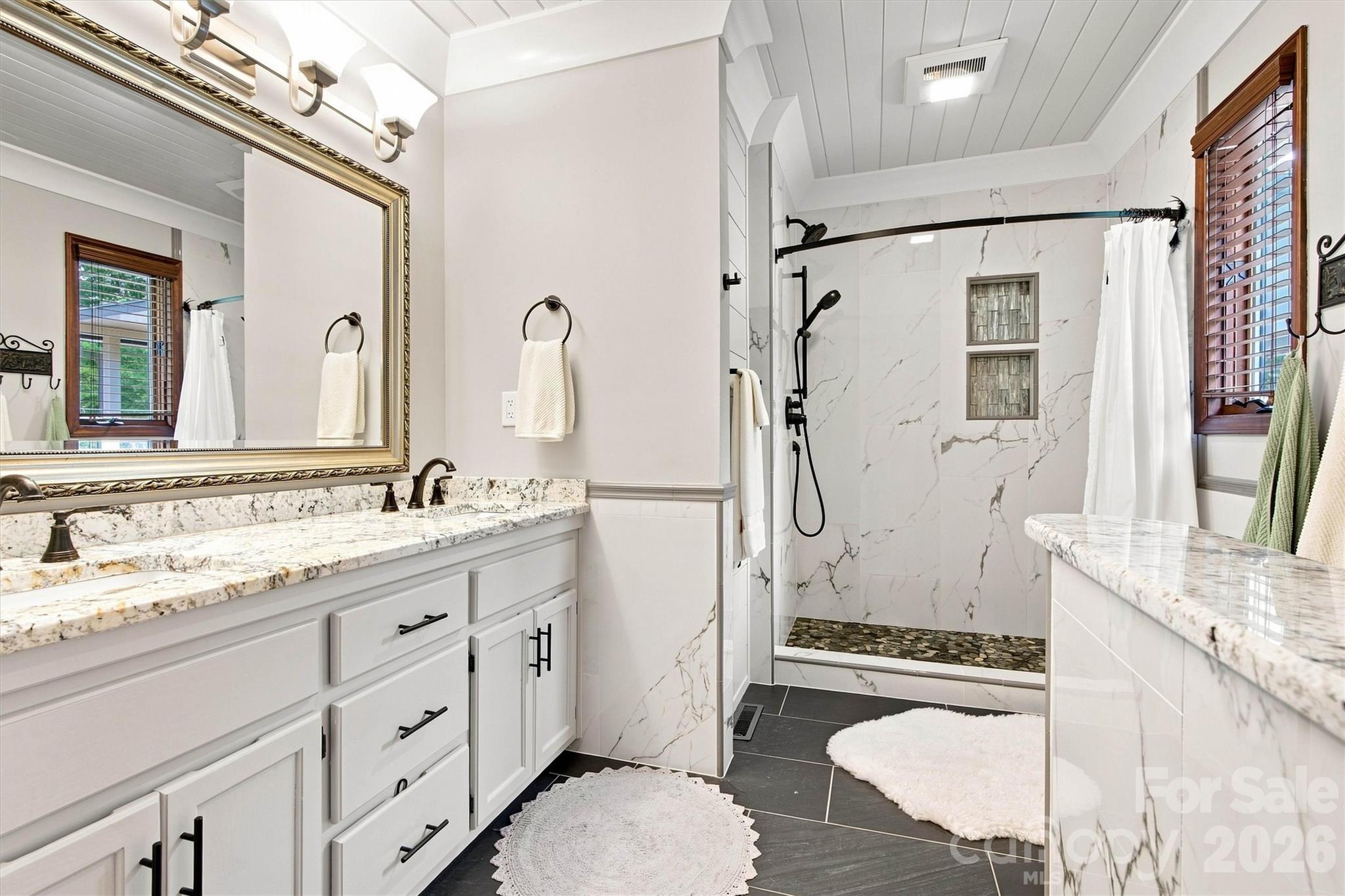 Primary Bath is gorgeous! Beautiful tile floors, white washed wood ceiling, gorgeous tile shower, granite countertops, with knee wall providing a bit of privacy. - 3867 Angie Drive, Denver