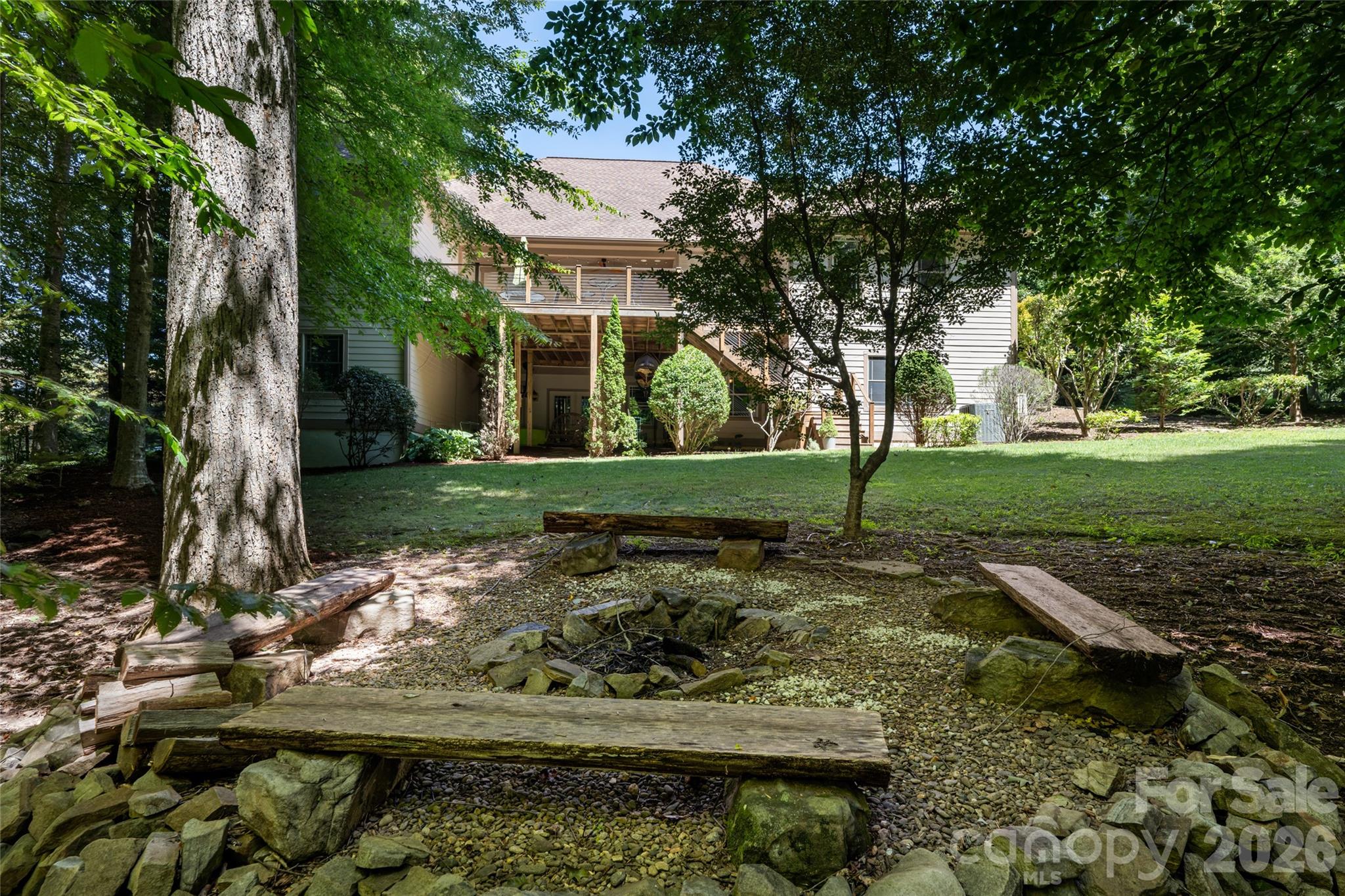 A large, private back yard with firepit, grass and shade, and upper porch with Ipe flooring and a hanging porch bed, partially covered, and basement access from under covered lower area with concrete pad. - 170 Cape Martin Circle, Hendersonville