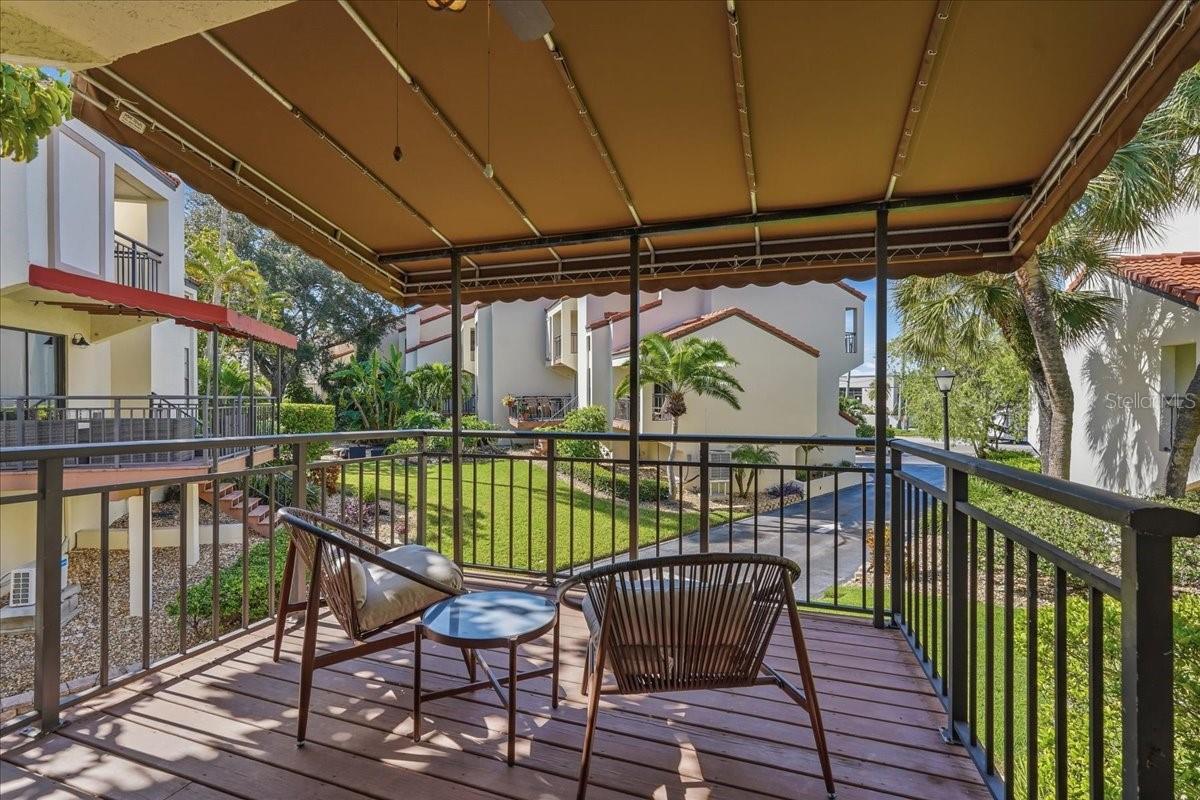 Private Covered Balcony: Elevated outdoor living space directly off the main great room, equipped with a large overhead canvas awning and integrated ceiling fan for maximum shade and comfort - 240 WINDWARD PSGE #702, CLEARWATER