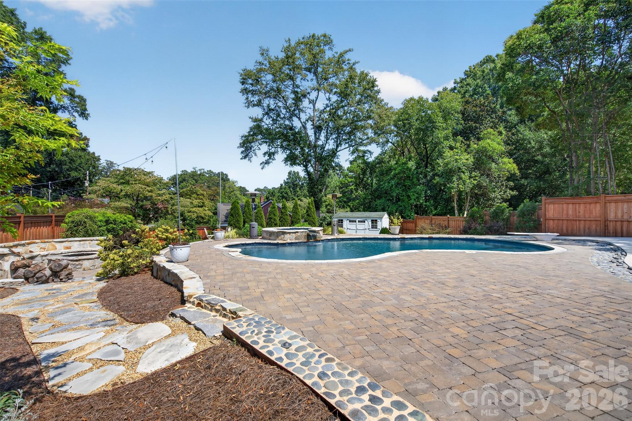 The backyard opens into a private outdoor retreat with a heated pool and hot tob, expansive paver patio, landscaped gathering areas, and a fire pit with stone seating surround nestled to the side. - 638 Carolina Avenue, Gastonia
