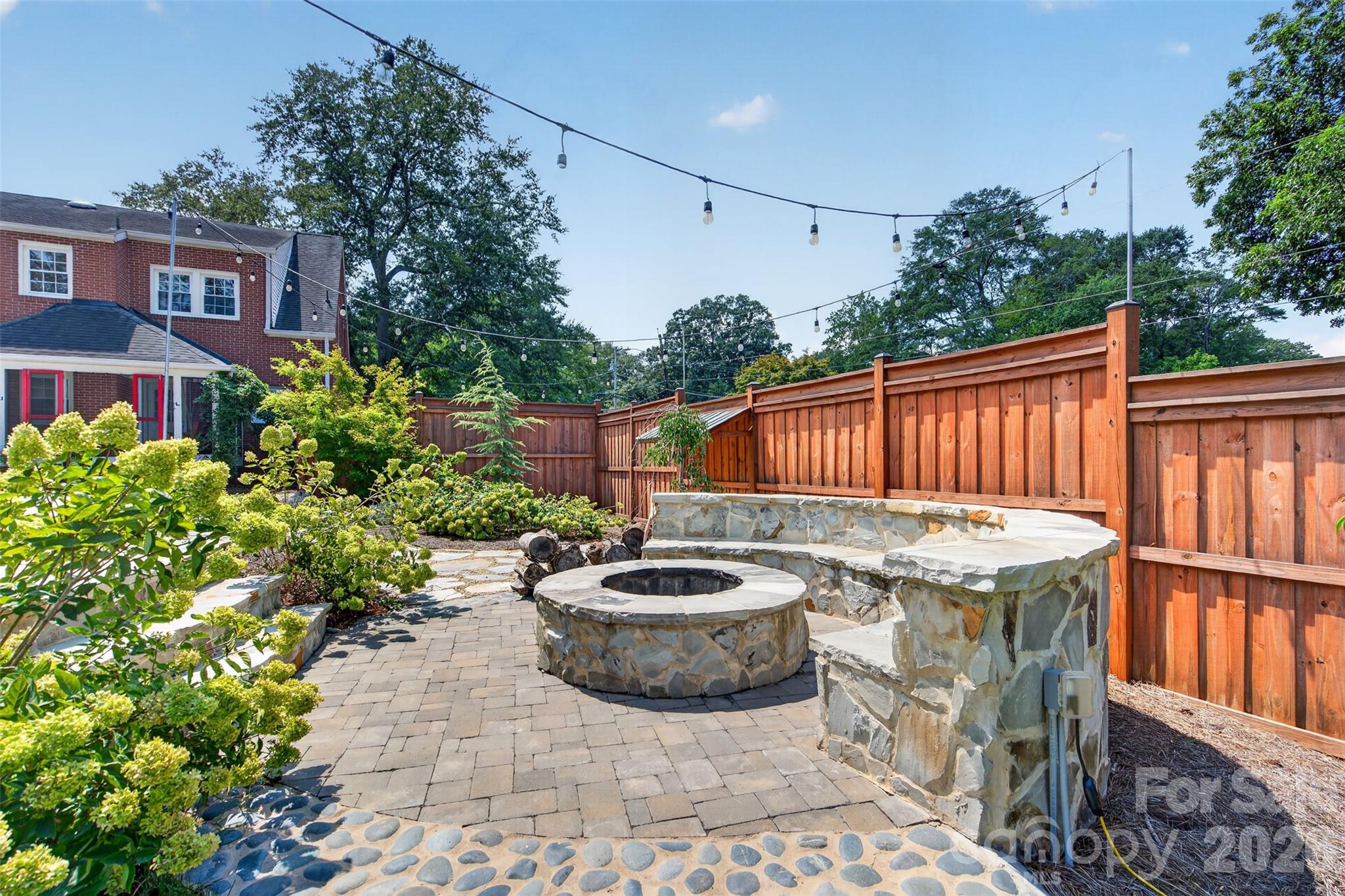 A closer look at the custom stone fire pit and built-in seating surrounded by beautiful mature landscaping and. Overhead string lighting adds another layer of charm to this inviting outdoor retreat. - 638 Carolina Avenue, Gastonia