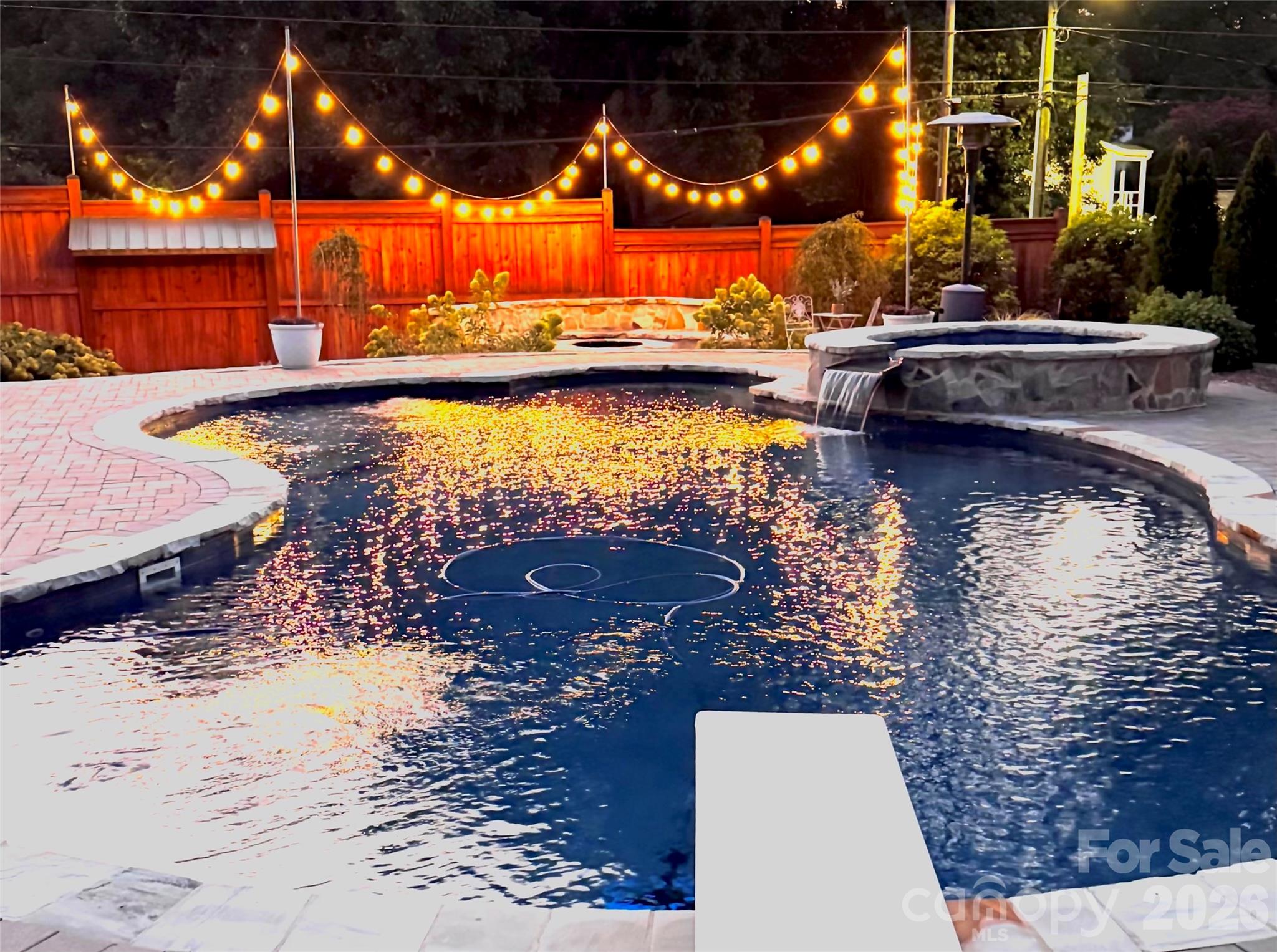An evening view captures the warm string lights reflected across the pool and the hot tub waterfall spillover in action. - 638 Carolina Avenue, Gastonia