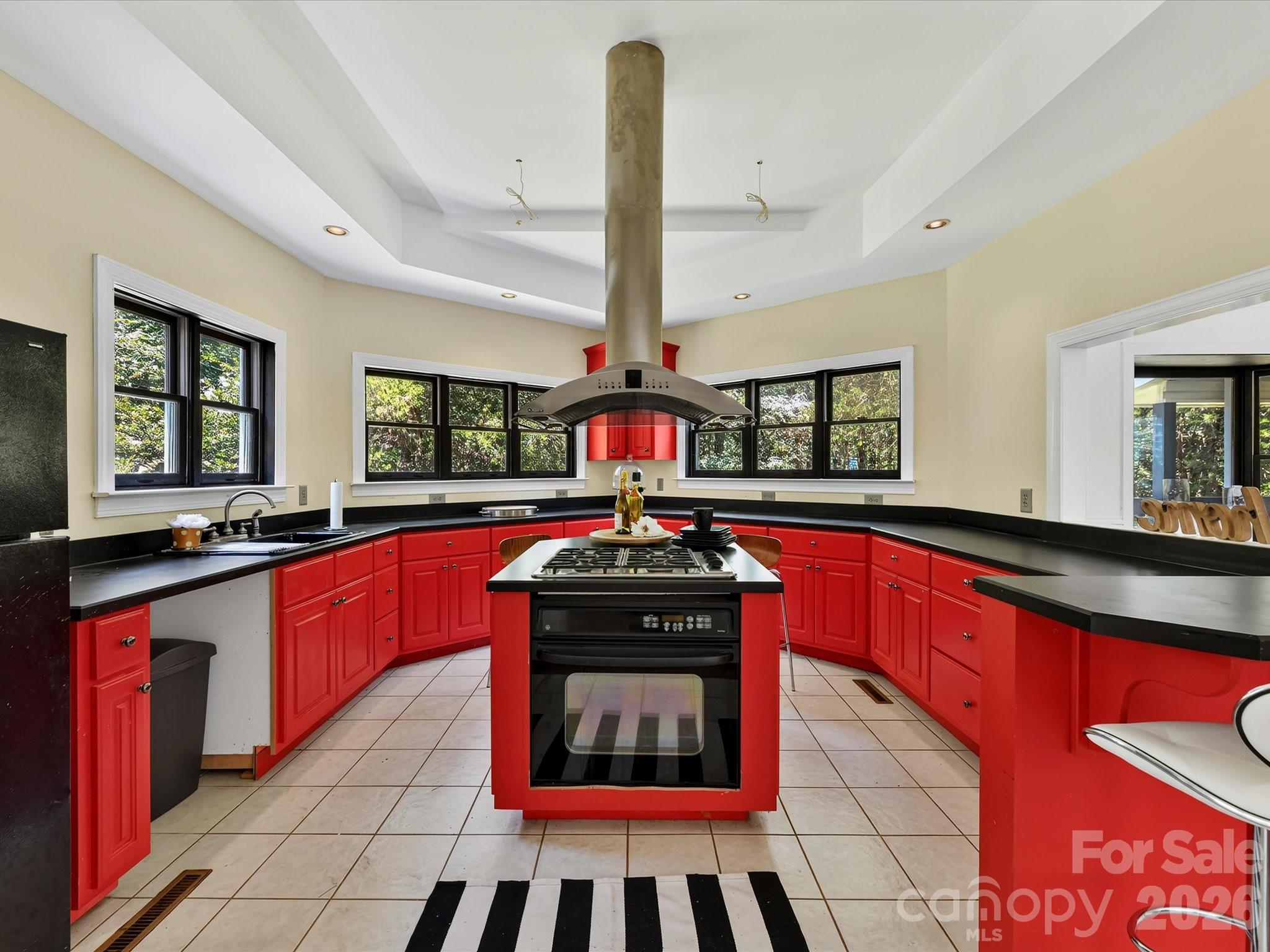 Spacious kitchen offers tile flooring, abundant cabinetry and counter space, a center island with cooktop, and windows overlooking the wooded property. - 9821 Harvest Lane, Davidson