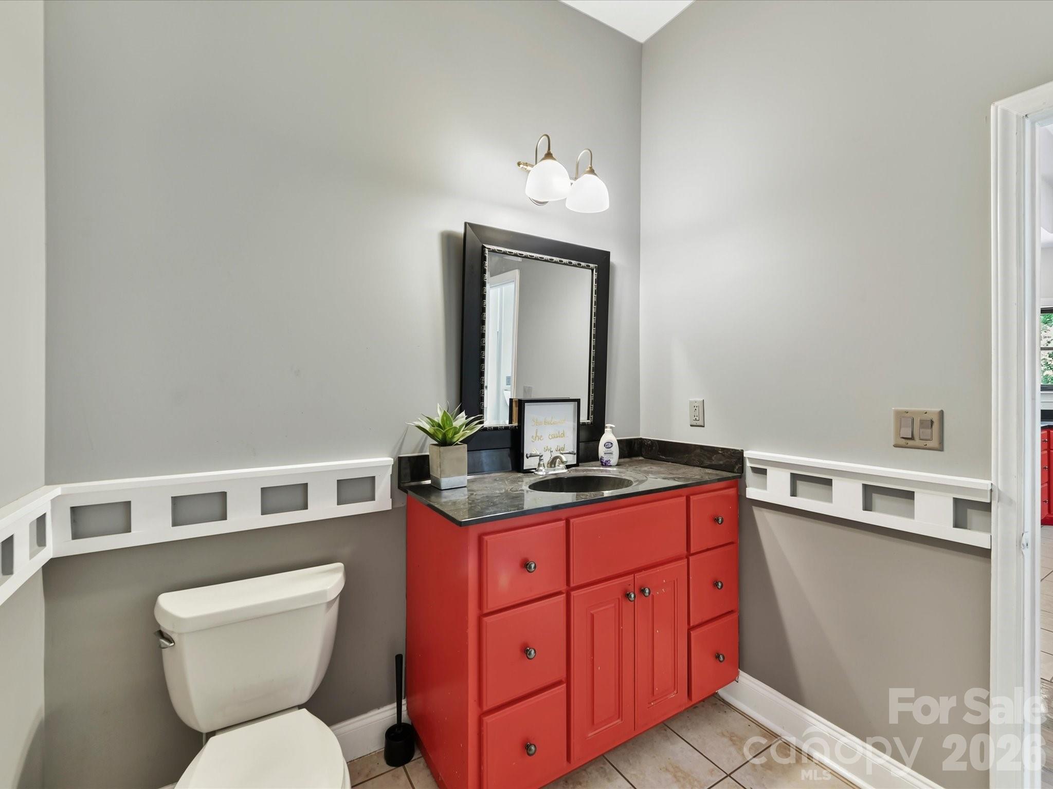 Convenient main-level powder room with tile flooring, ample vanity storage, and decorative trim details. - 9821 Harvest Lane, Davidson