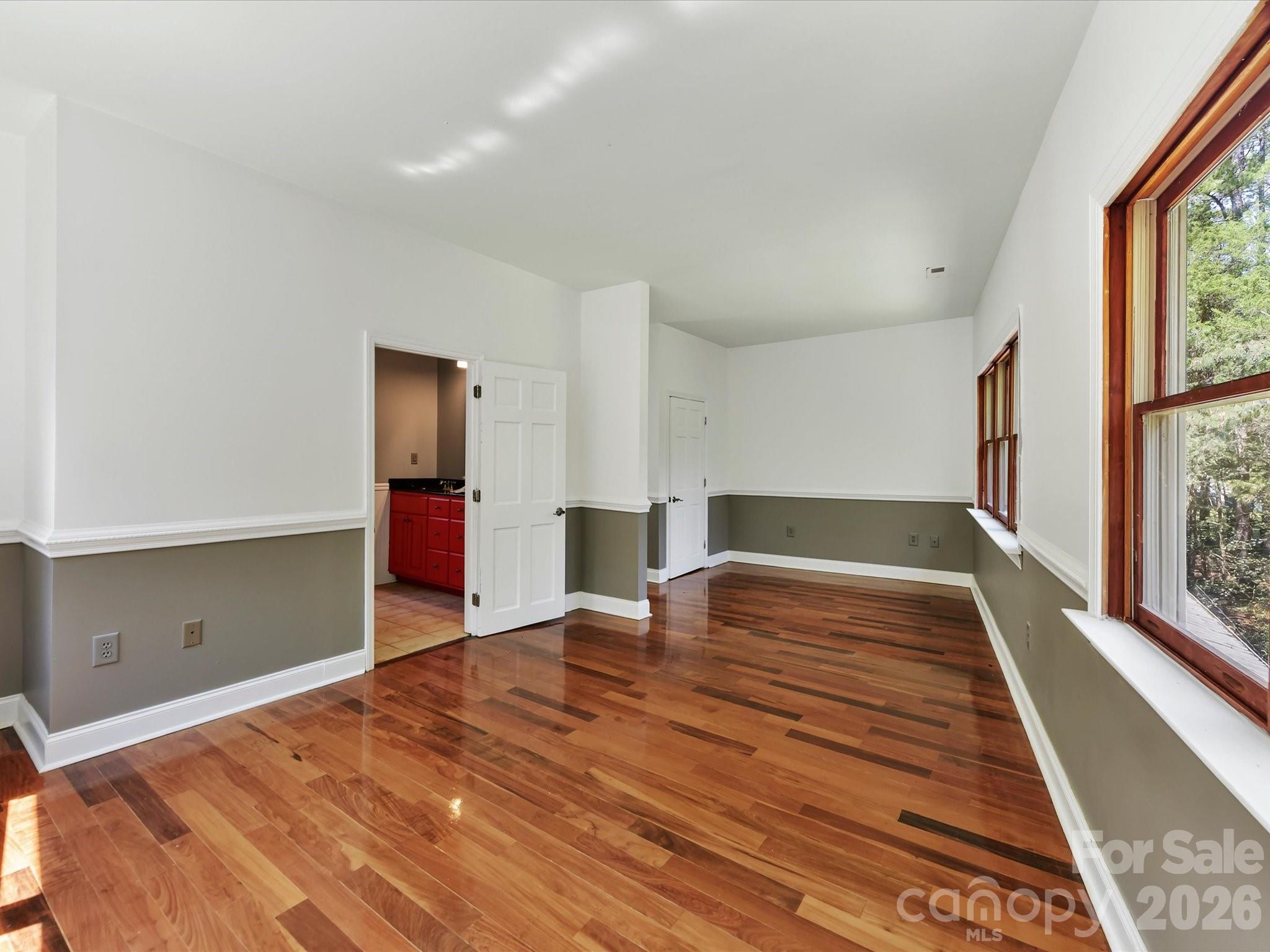 Spacious primary suite features gleaming Brazilian hardwood floors, abundant natural light, and peaceful wooded views from multiple oversized windows. - 9821 Harvest Lane, Davidson