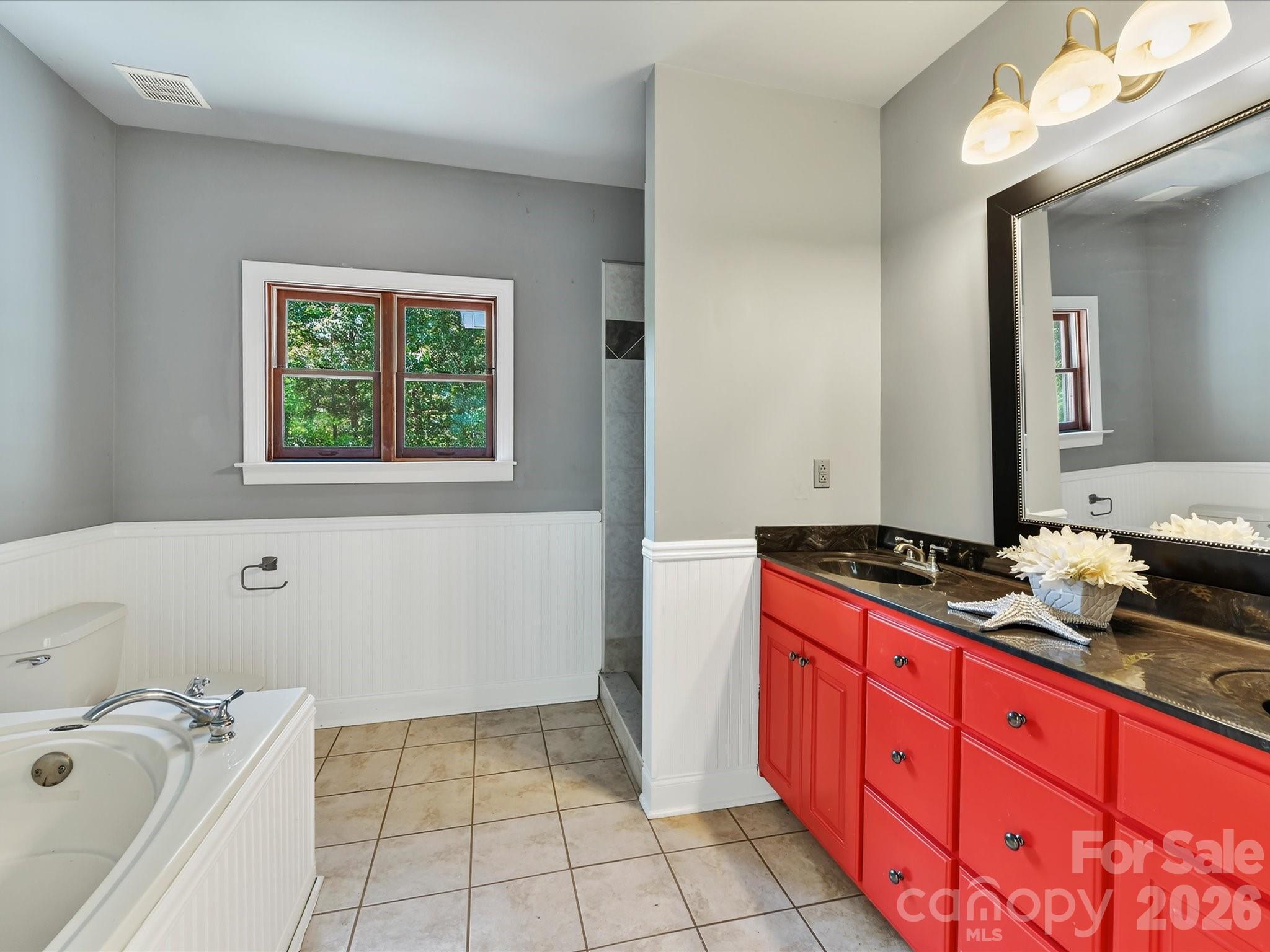 Primary bath features tile flooring, a soaking tub, separate shower, spacious vanity, and natural light from a wooded-view window. - 9821 Harvest Lane, Davidson