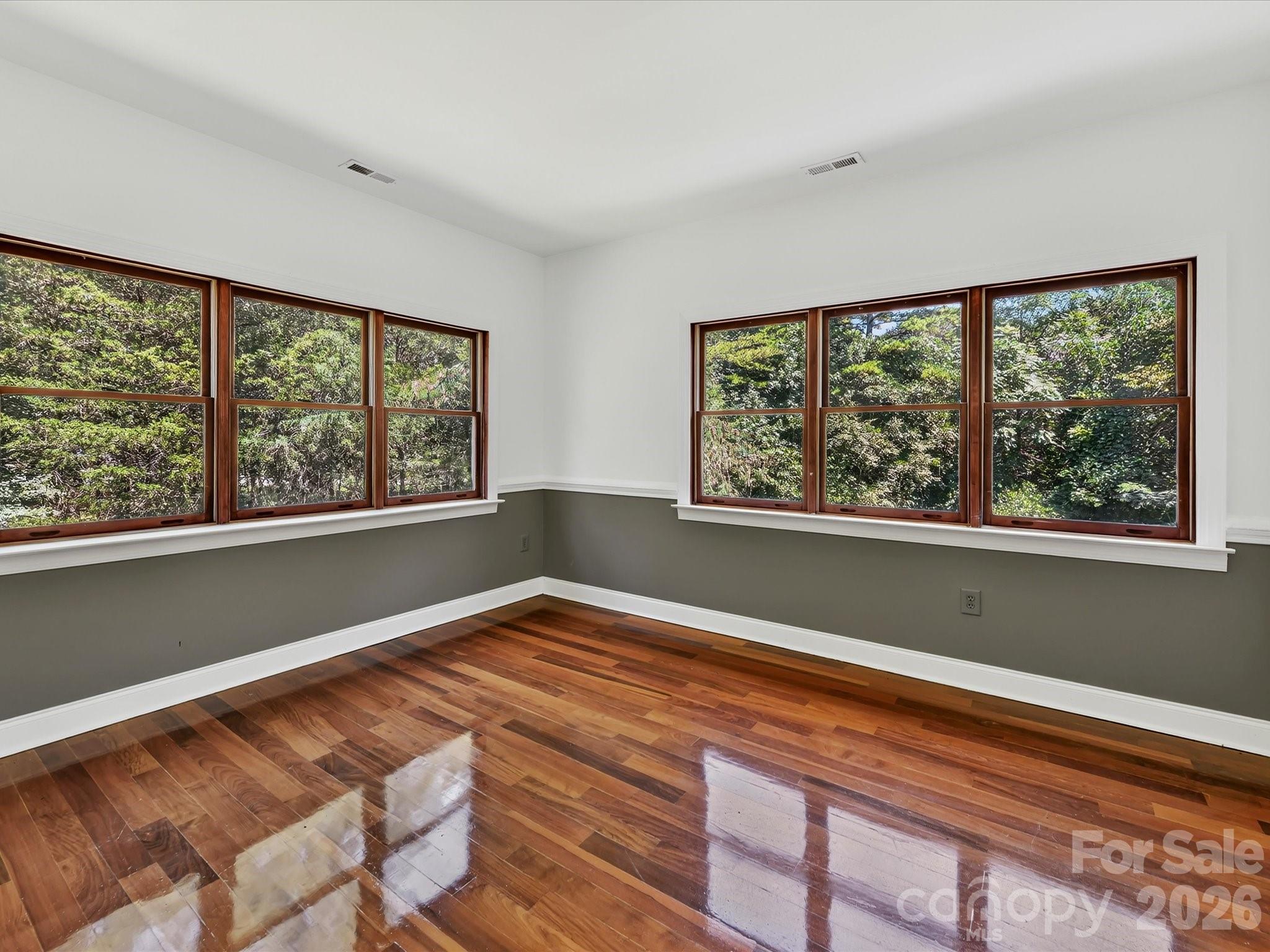 Bright secondary bedroom showcases Brazilian hardwood floors, multiple windows, and serene views of the surrounding Davidson woods. - 9821 Harvest Lane, Davidson
