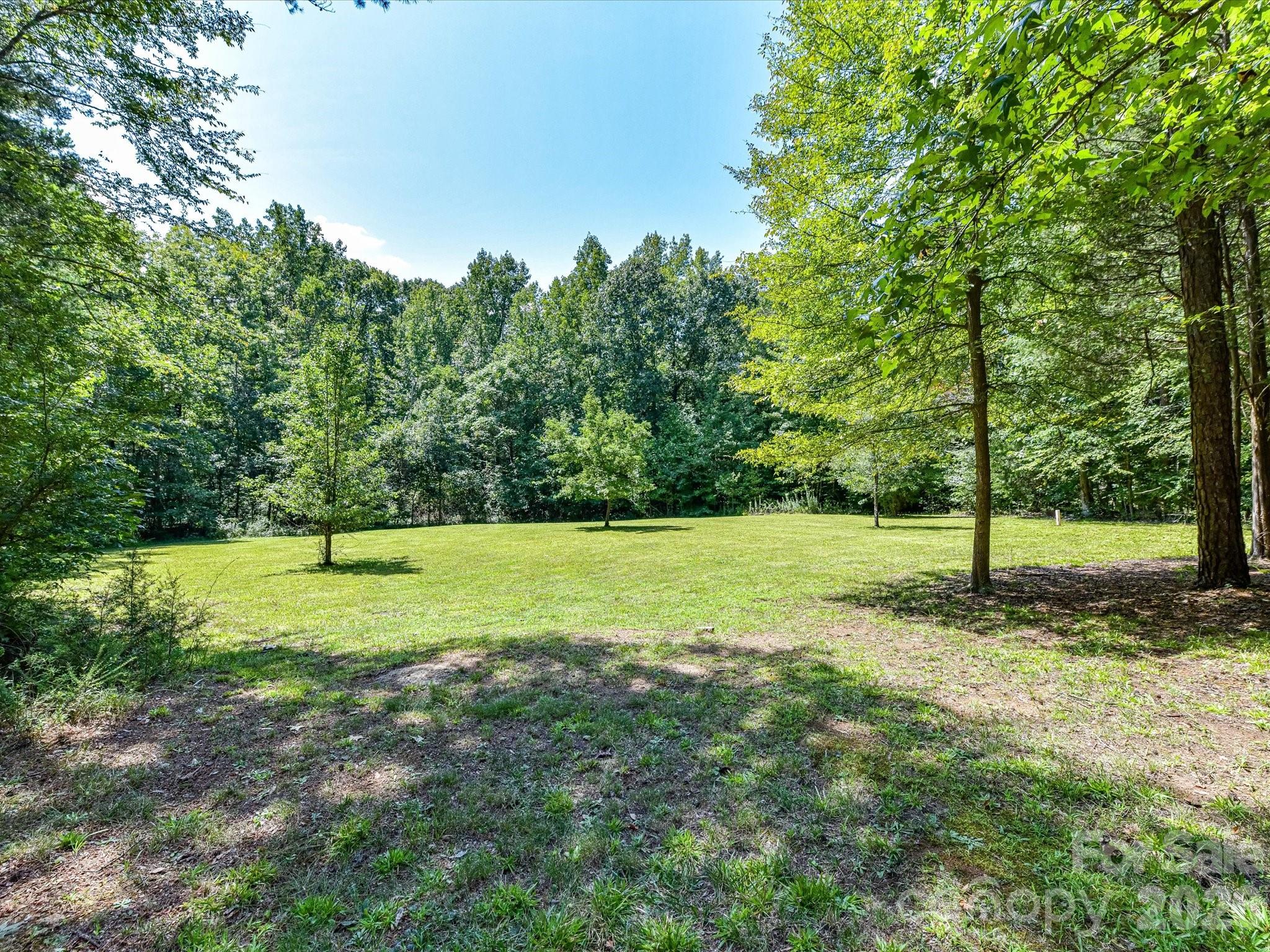 Expansive backyard offers a large open lawn surrounded by mature trees, creating a peaceful and private outdoor setting. - 9821 Harvest Lane, Davidson