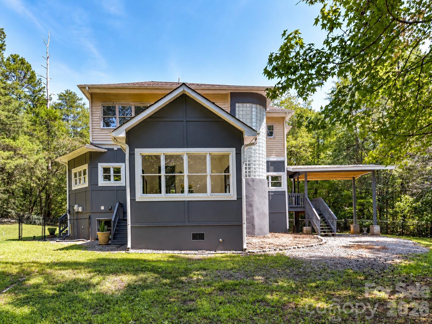 Rear view highlights the home’s distinctive architecture, expansive windows, covered outdoor living space, and private wooded backdrop. - 9821 Harvest Lane, Davidson