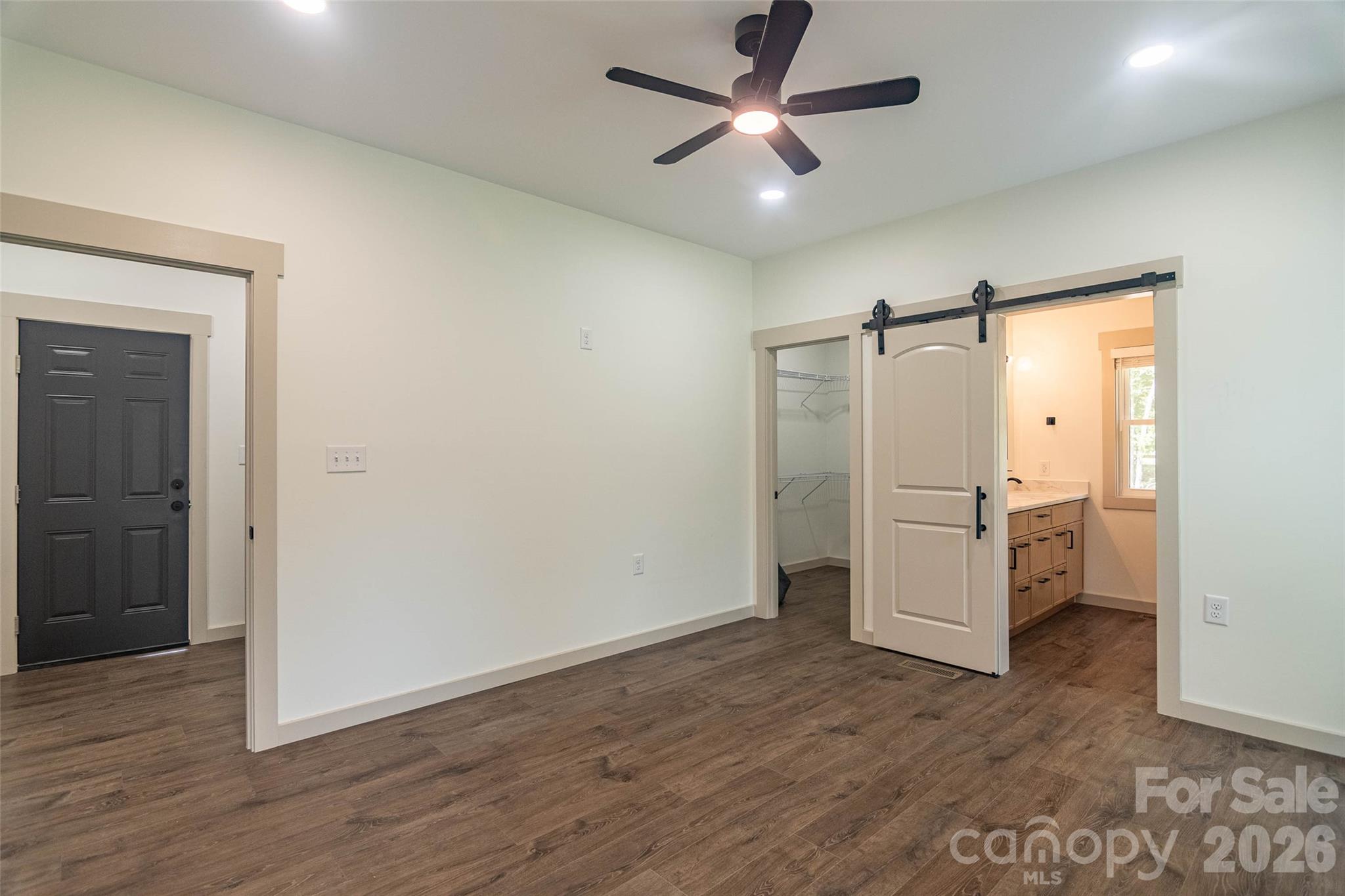 The primary bedroom suite has walk in closet, plenty of space, and a very cool barn door to the primary bathroom! Brown door takes you right to the garage, and the laundry room is just to the right there. - 98 Lexxi Lane, Tryon