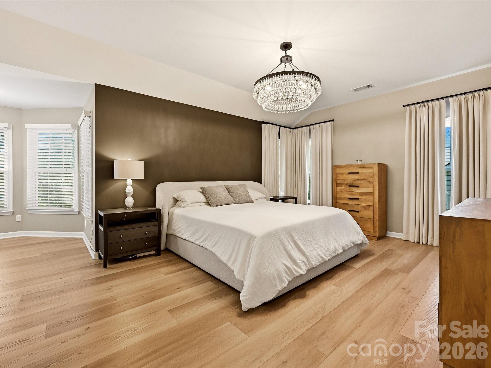 Spacious primary bedroom features wood-look vinyl plank flooring, abundant natural light, and generous proportions for a complete bedroom suite. - 19706 Valiant Way, Cornelius
