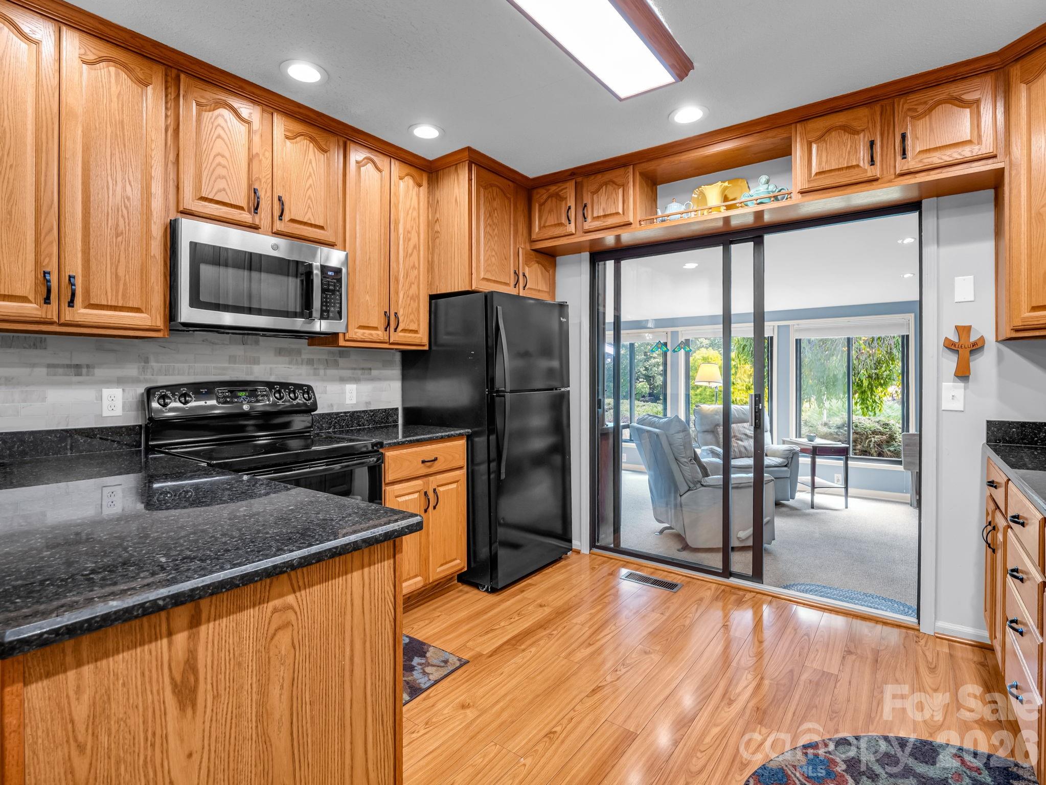 Kitchen offers granite counters and updated backsplash, wood floors and leads to four-seasons sunroom which overlooks the lake - 31 Willow Way, Hendersonville