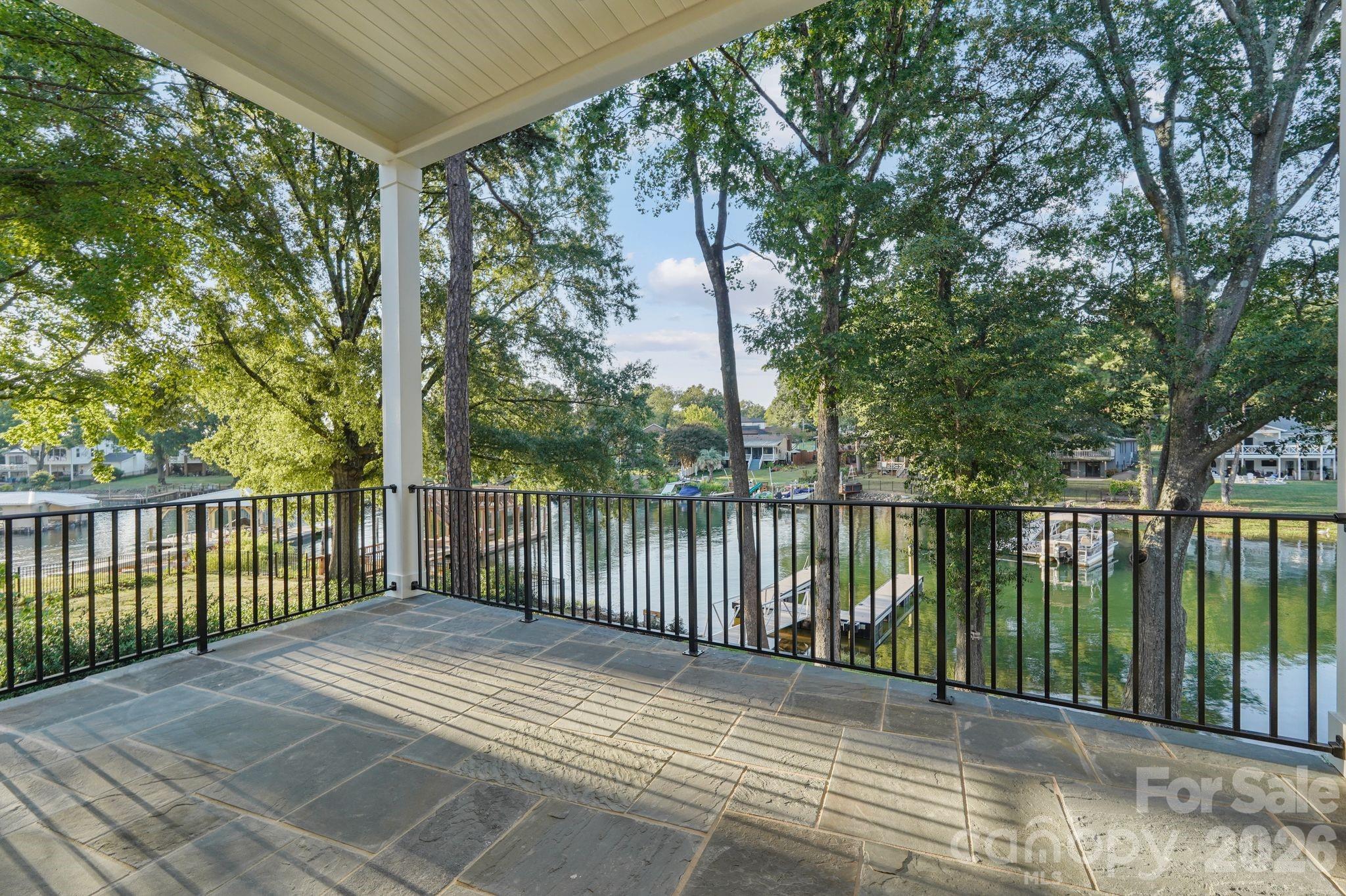 Main-level porch featuring soaring 12' tongue-and-groove ceilings, sleek steel railings, and beautiful water views. - 21216 Rio Oro Drive, Cornelius