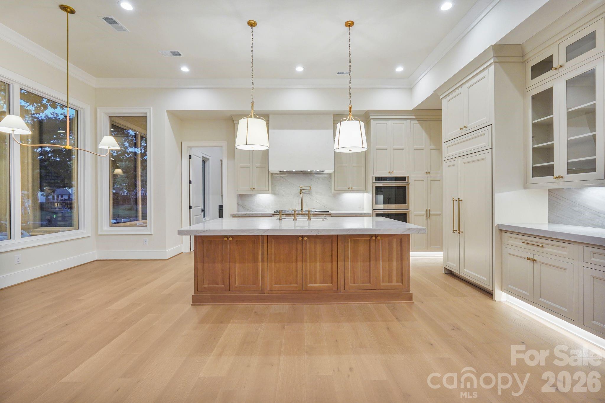 White oak island accented by two oversized pendant lights, intentionally positioned to preserve a clean sightline to the Venetian plaster hood. - 21216 Rio Oro Drive, Cornelius