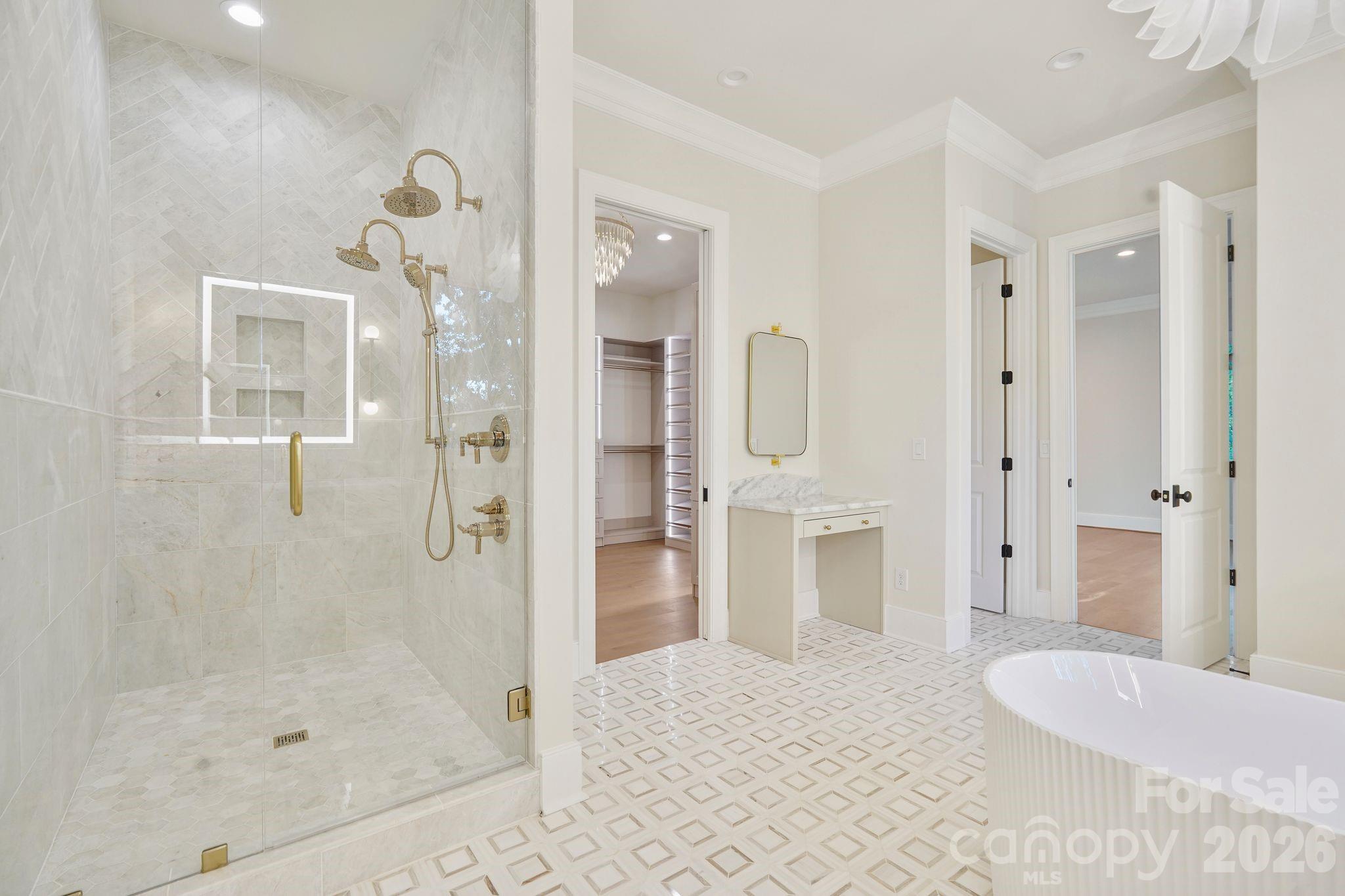 Luxurious marble shower featuring dual shower heads, floor-to-ceiling tile, and expansive frameless glass, complemented by a dedicated makeup vanity for a truly spa-inspired primary bath. - 21216 Rio Oro Drive, Cornelius