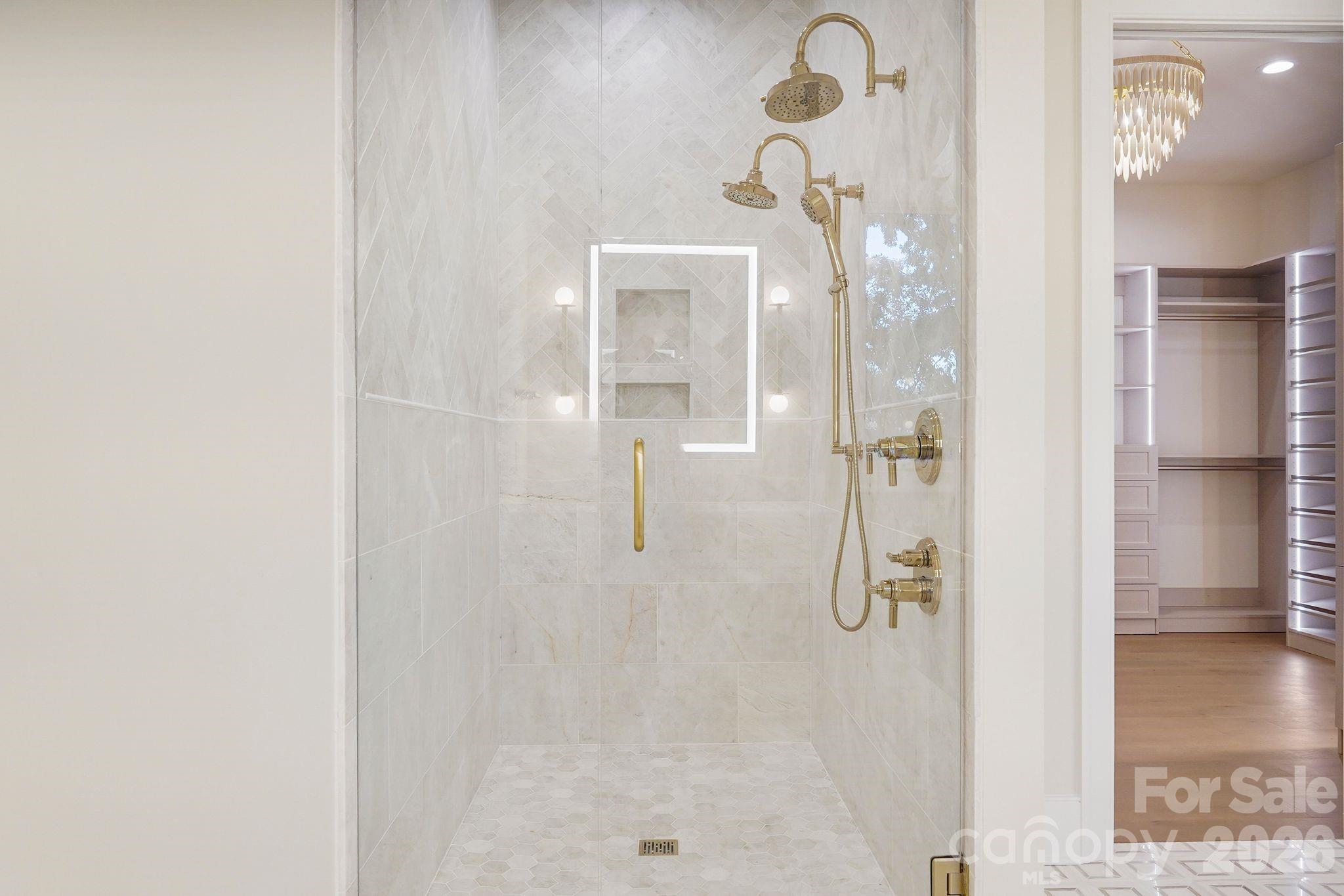 Showstopping marble shower featuring dual shower heads, floor-to-ceiling tile, and expansive frameless glass, creating a luxurious spa-like experience within the primary suite. - 21216 Rio Oro Drive, Cornelius