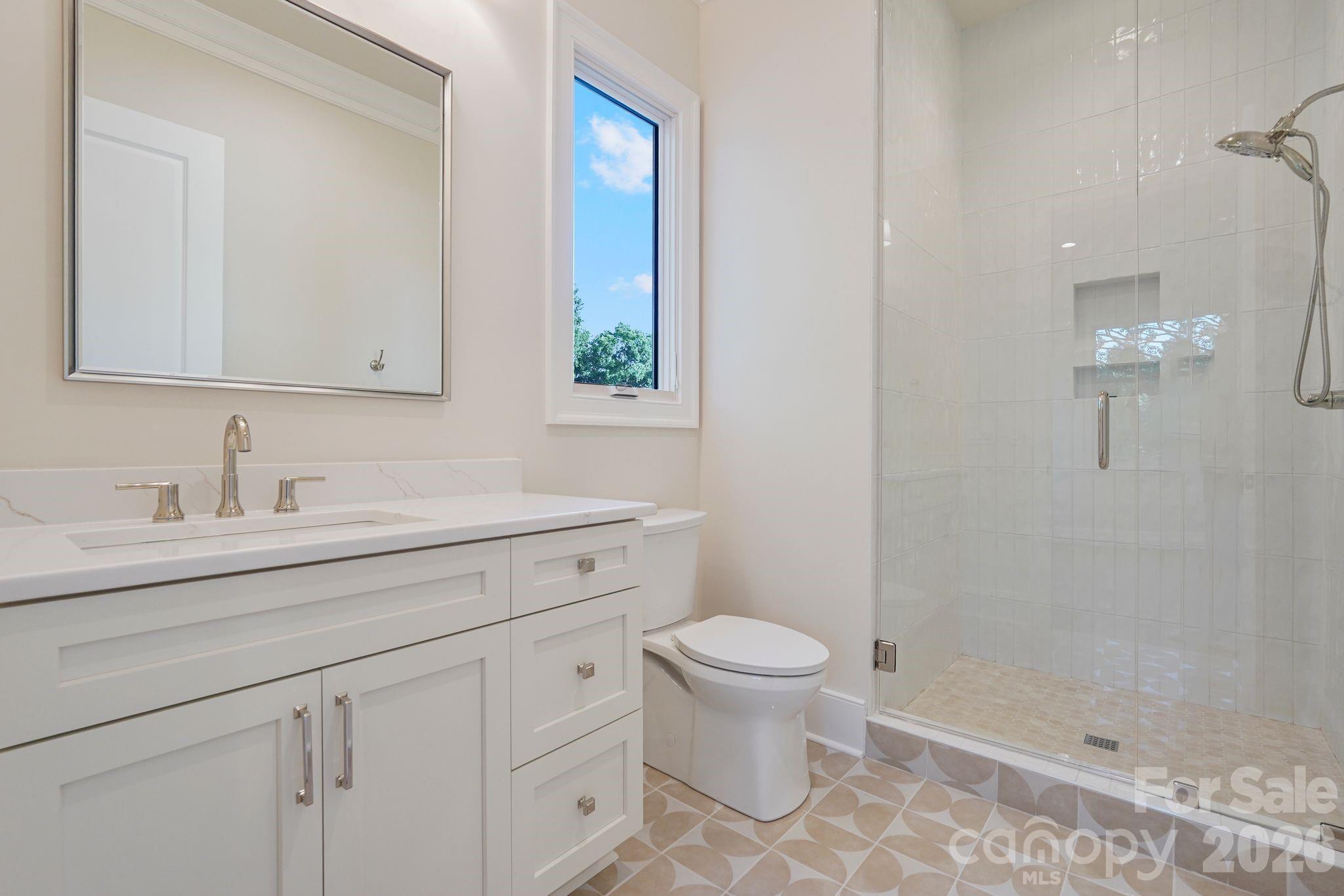 Bedroom 2 ensuite bath features floor-to-ceiling tile and a thoughtfully placed window that fills the space with natural light, creating a bright, elevated finish. - 21216 Rio Oro Drive, Cornelius