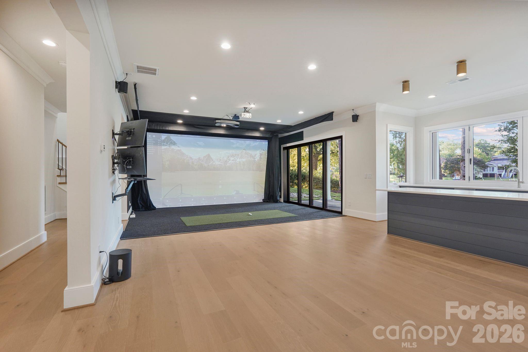 Open view of the golf simulator and entertainment space, featuring a quad-stack sliding glass door that opens to the covered porch for seamless indoor-outdoor living. - 21216 Rio Oro Drive, Cornelius
