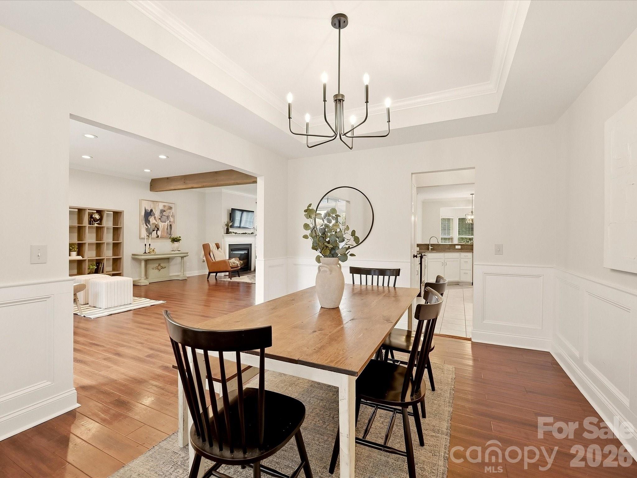 The elegant dining room features warm wood floors, classic wainscoting, a tray ceiling, and a modern chandelier with an open connection to the main living spaces. - 16006 Lavenham Road, Huntersville