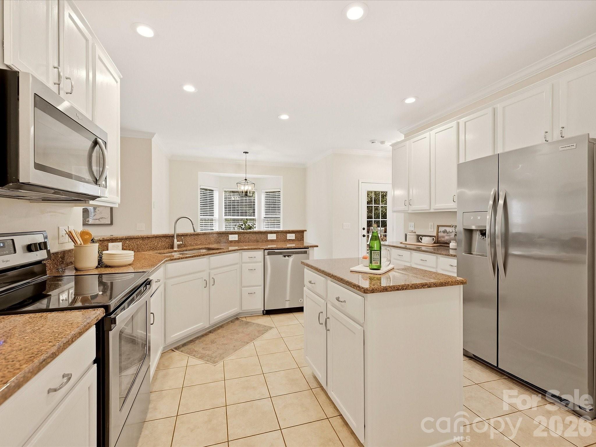 The bright kitchen features crisp white cabinetry, granite countertops, stainless steel appliances, a center island, and an open layout that connects easily to the surrounding living spaces. - 16006 Lavenham Road, Huntersville