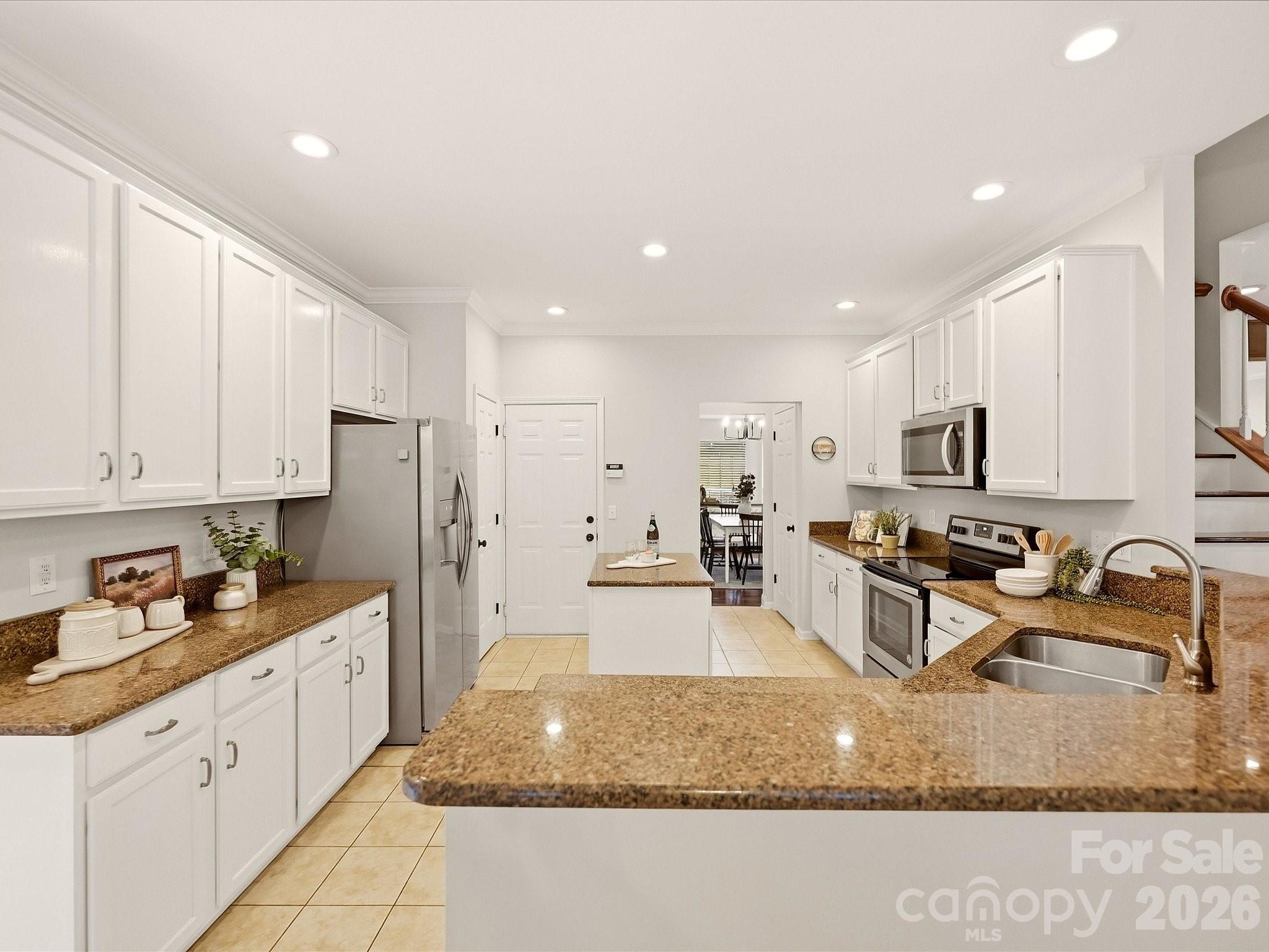 The bright kitchen features crisp white cabinetry, generous counter space, stainless steel appliances, a center island, and an adjoining breakfast area filled with natural light. - 16006 Lavenham Road, Huntersville