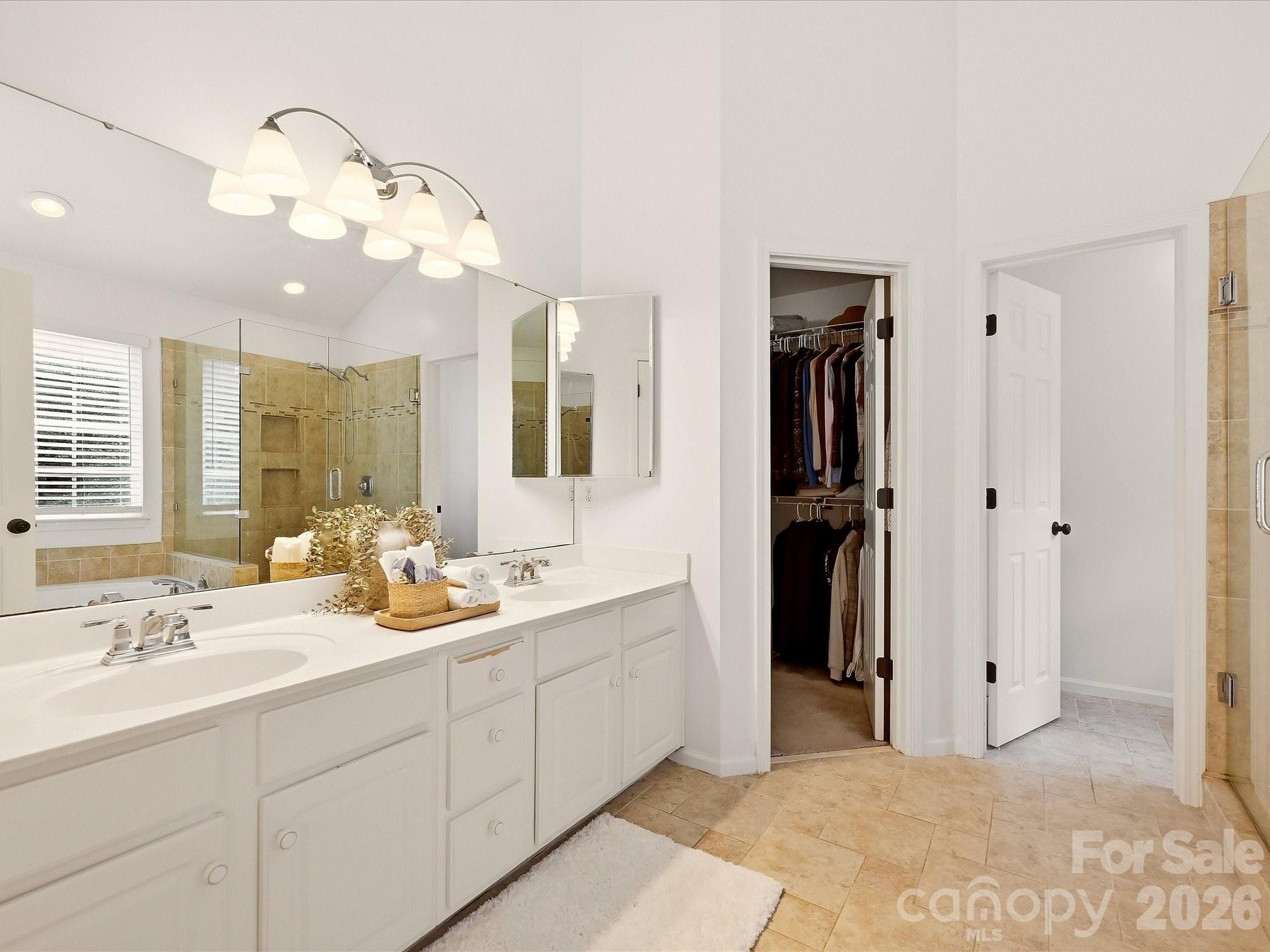 The primary bath features dual vanities, a garden tub, a separate glass-enclosed shower, and abundant natural light for a bright, relaxing retreat. - 16006 Lavenham Road, Huntersville
