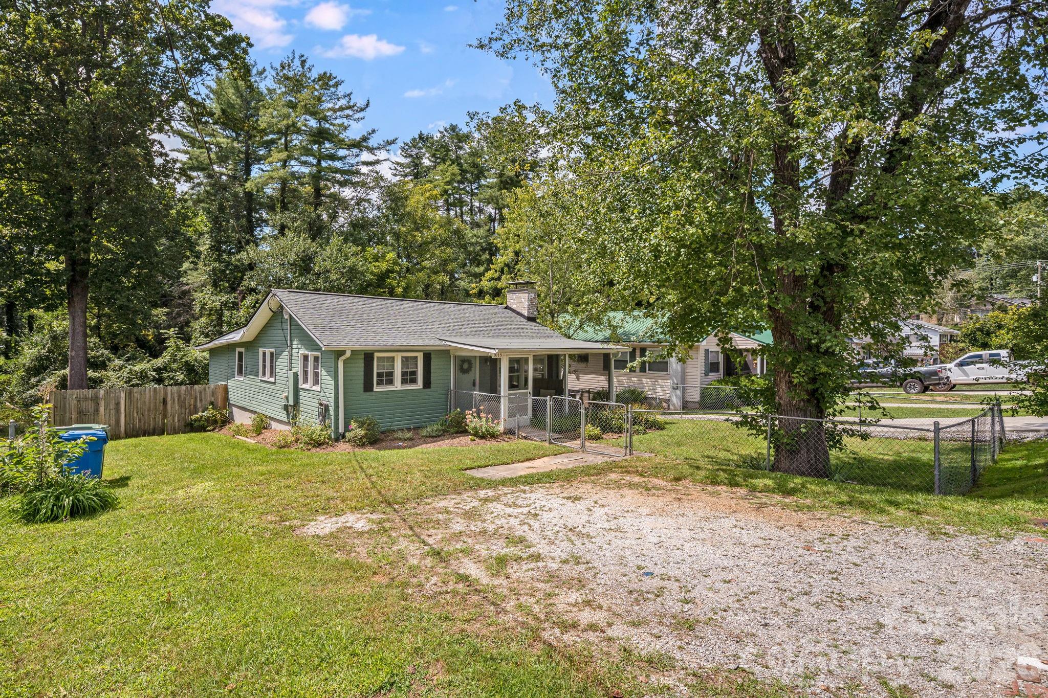 This view shows the driveway, fenced front yard, privacy fence for the backyard, and lovely large mature trees. - 1015 Mountain View Street, Hendersonville