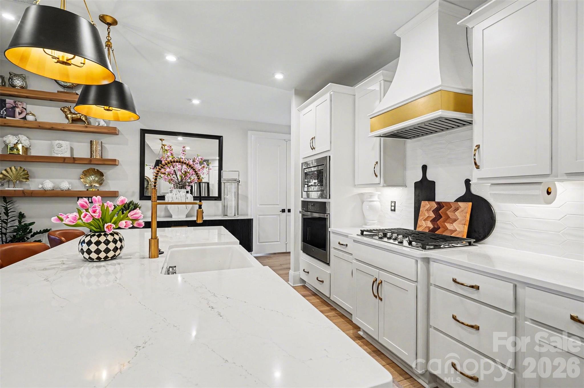 A big farmhouse sink in the island, a gold faucet, and quartz counters. The gas cooktop is right across from it, so you never have to leave the conversation while you cook. - 8027 Longwaters Court, York