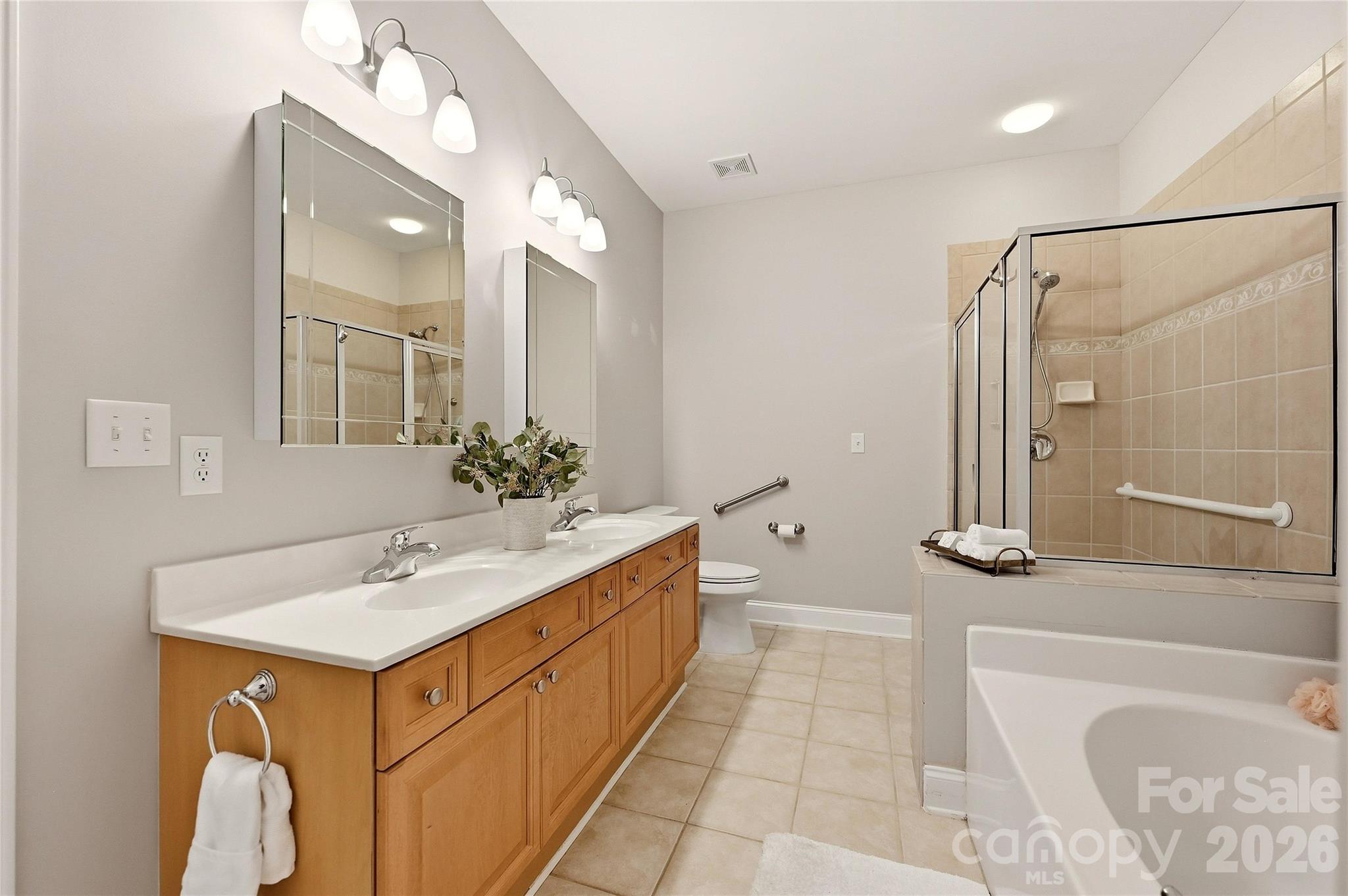 Primary bathroom features a long dual-sink vanity, tile flooring, garden tub, separate shower, and accessibility grab bars. - 9009 Rosalyn Glen Road, Cornelius