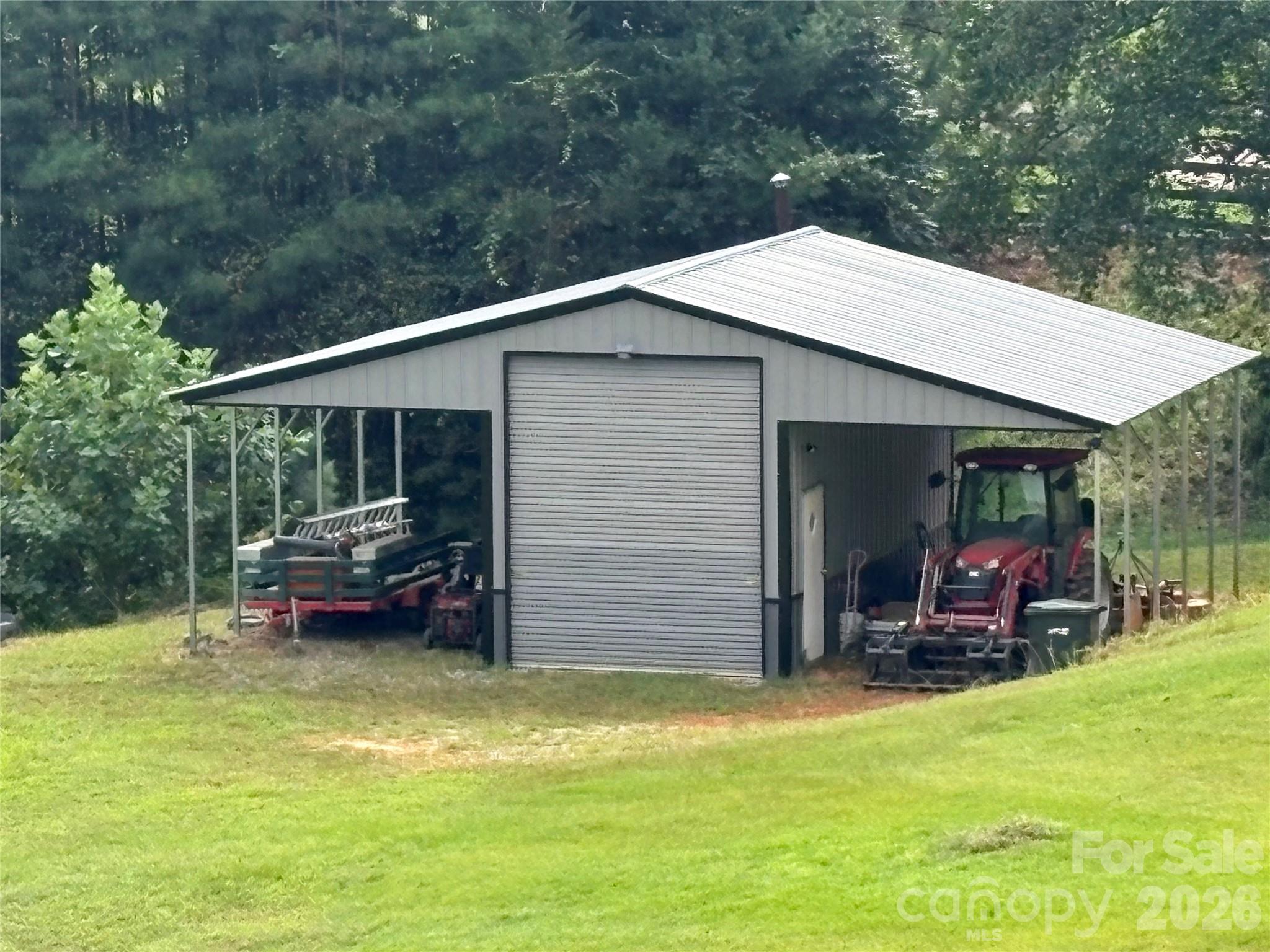 Metal building/tractor shed with two large open bays and a 10' wide x 12' tall roll up door. Concrete slab floor in the enclosed space makes it a great workshop, or use this space to store a horse trailer or RV. Overhangs are 12' wide by 10' high. - 27 & 56 Troy Lane, Tryon