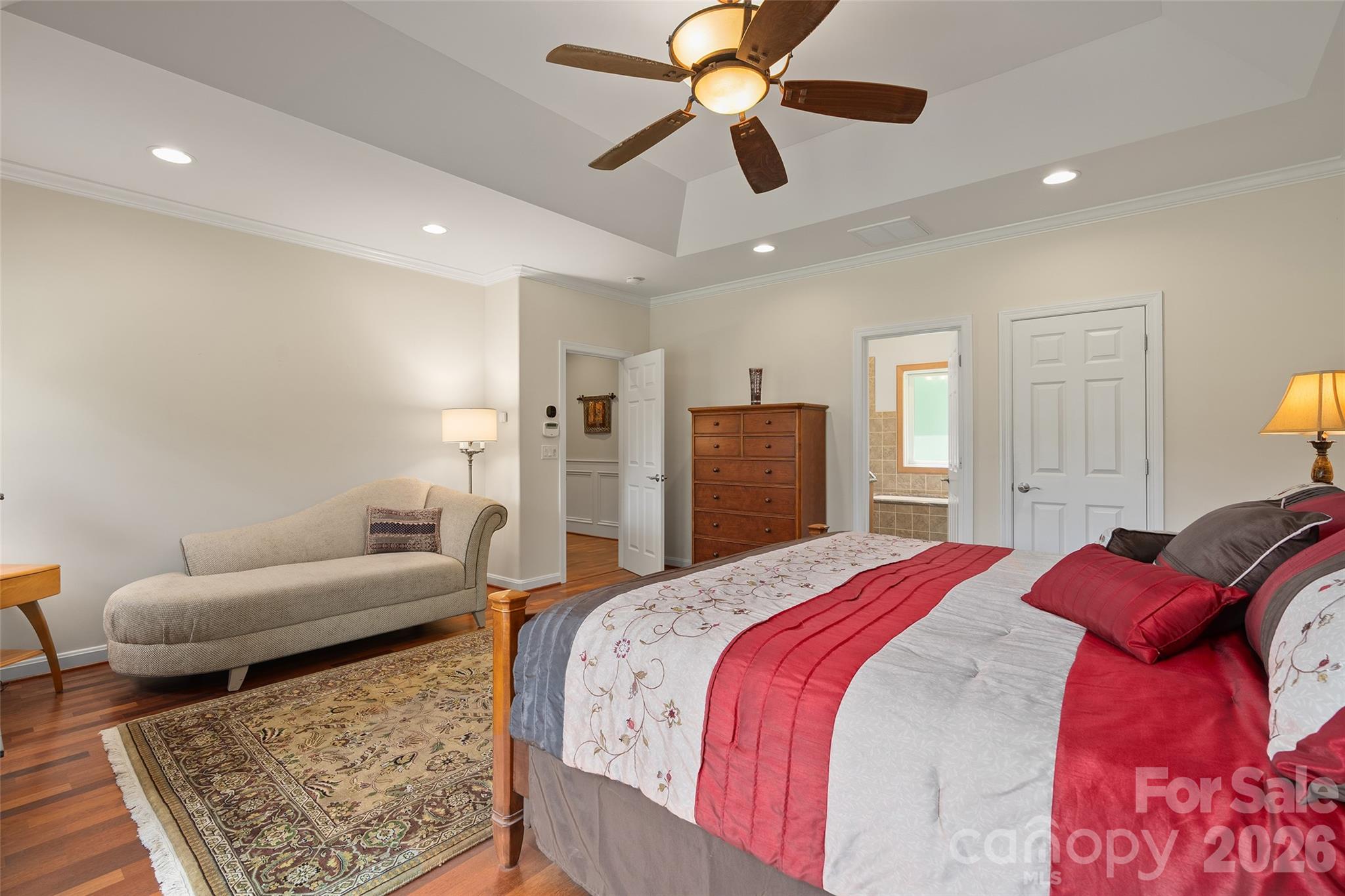 Generously sized primary bedroom with tray ceiling and warm hardwood flooring. - 174b Marina Cove, Waynesville