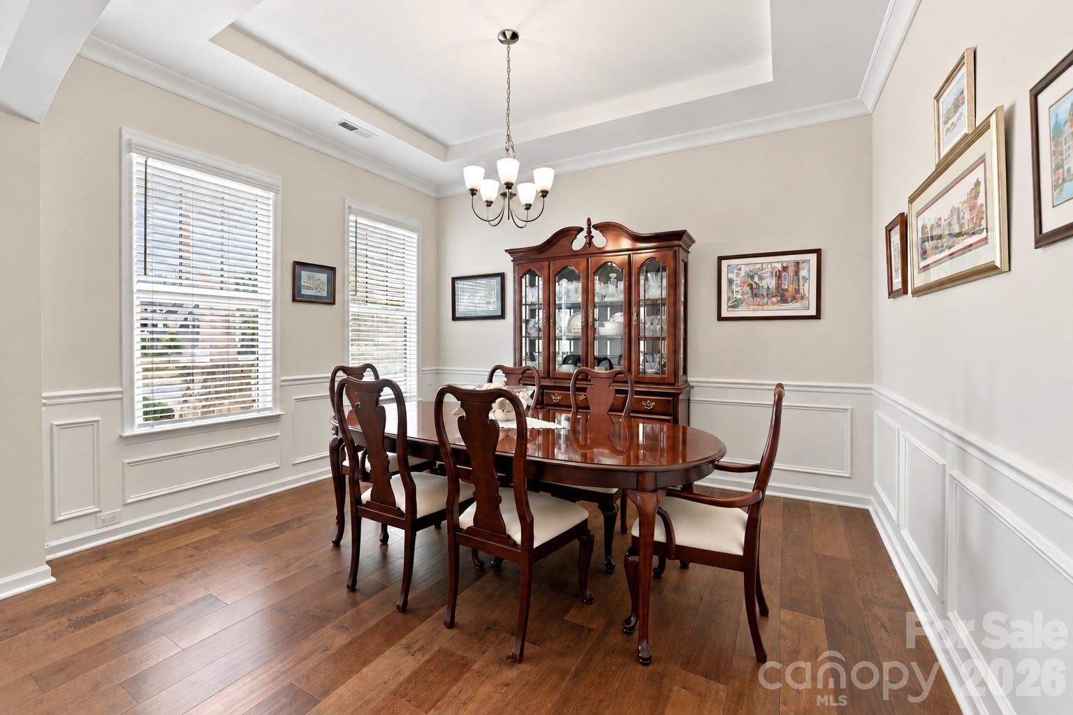 Elegant formal dining room with wide plank hardwood floors, tray ceiling, crown molding and detailed picture-frame wainscoting. Space to bring everyone together for holiday feasts, celebrations and memorable dinners. - 8504 Hope Run Court, Indian Land