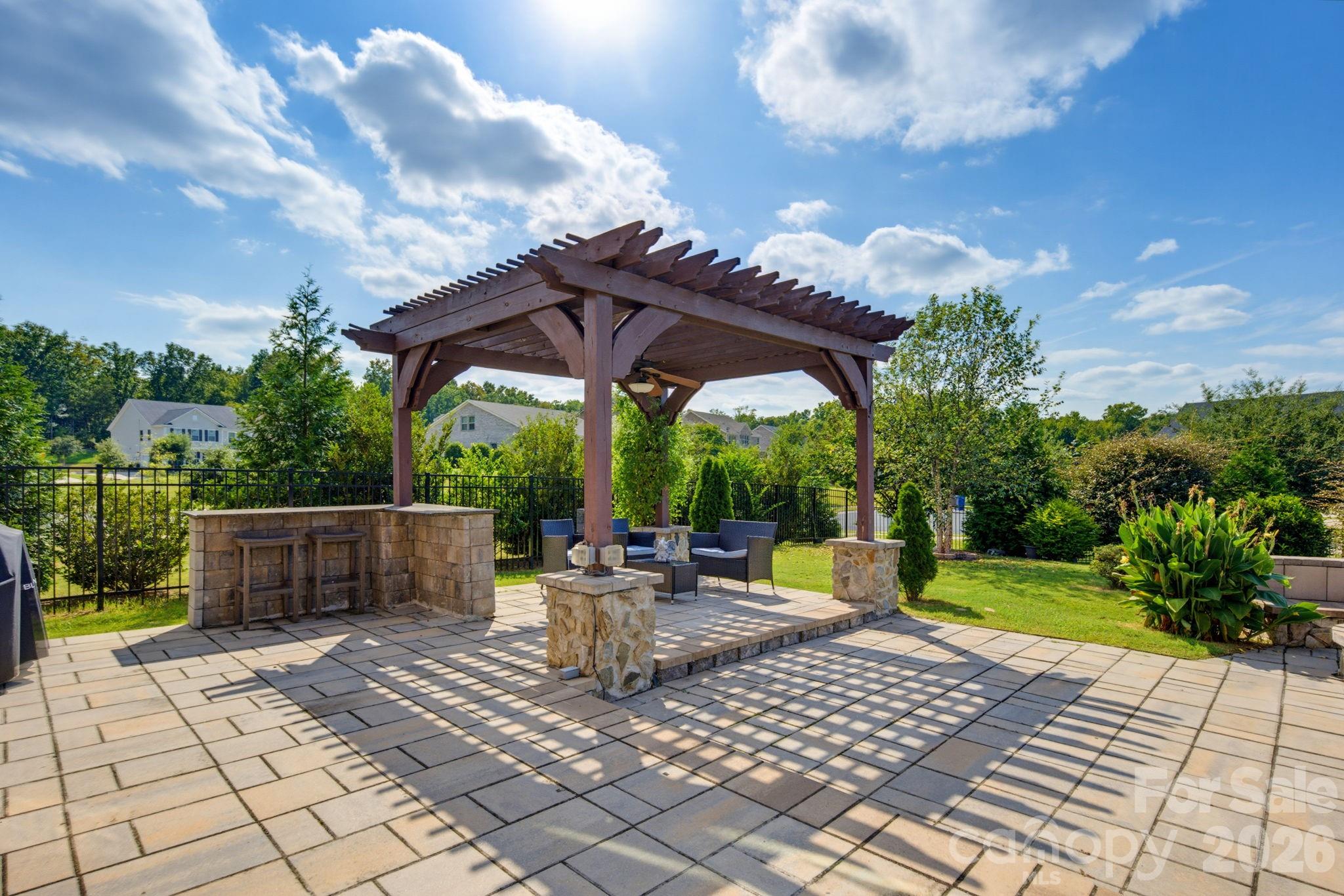 A wide patio view shows the pergola, built-in serving area, and open space for hosting family and friends. - 8315 Breton Way, Harrisburg