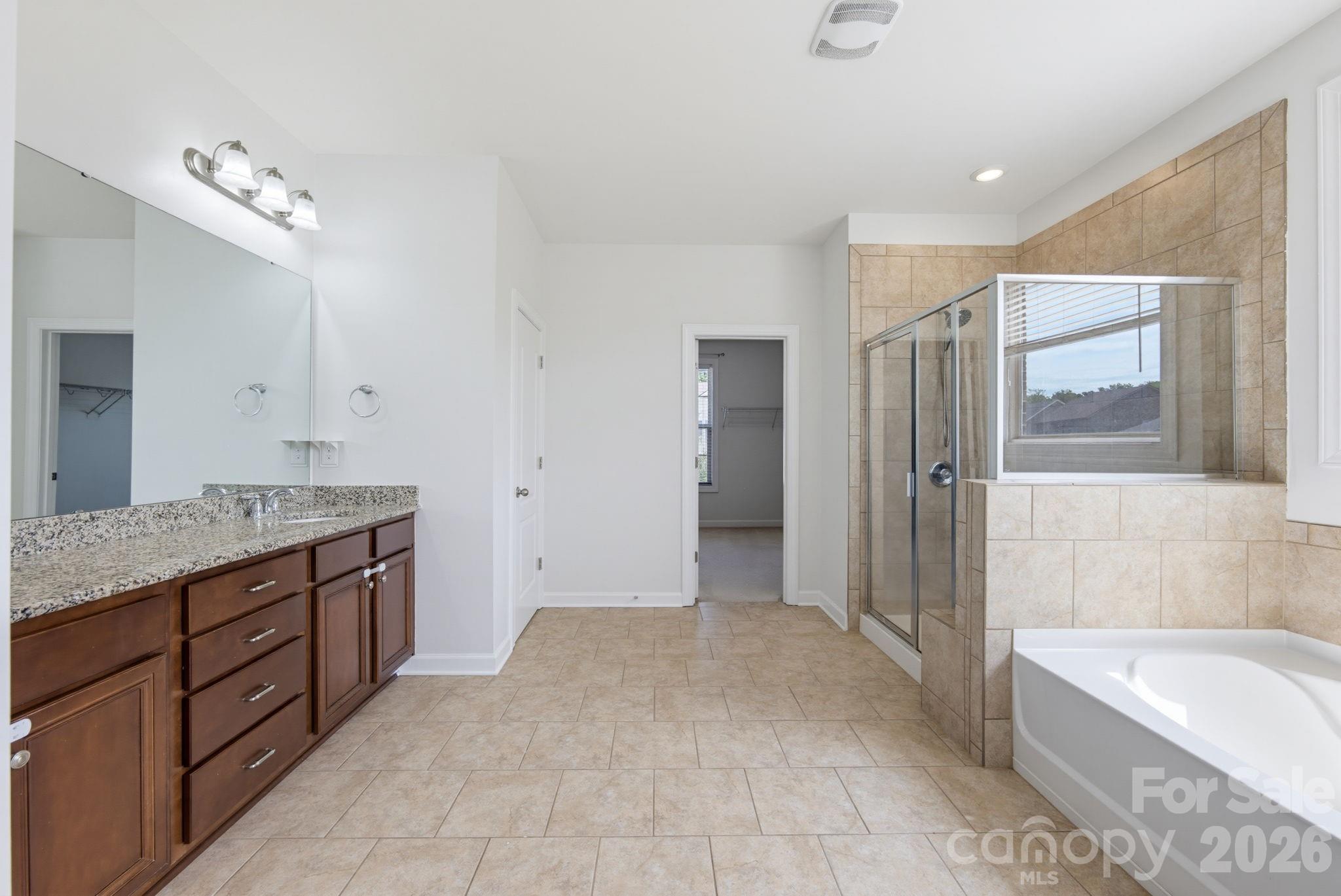 The spacious primary bath features a long dual-sink vanity, tiled floors, a walk-in shower, and a separate soaking tub. - 8315 Breton Way, Harrisburg