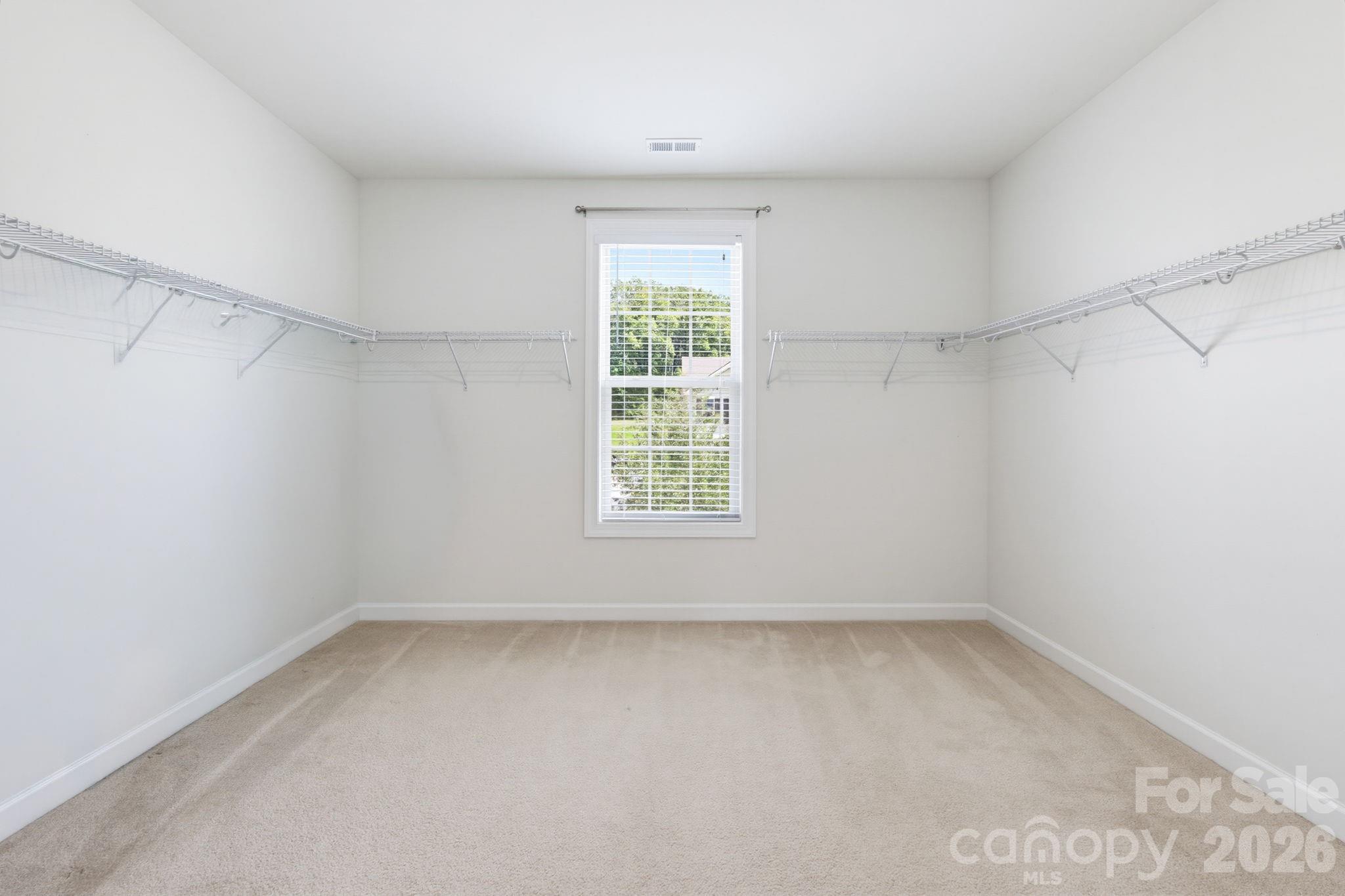 The unstaged view reveals the impressive scale of the primary closet, with abundant hanging space, an oversized footprint, and a window that brings natural light into the room. - 8315 Breton Way, Harrisburg