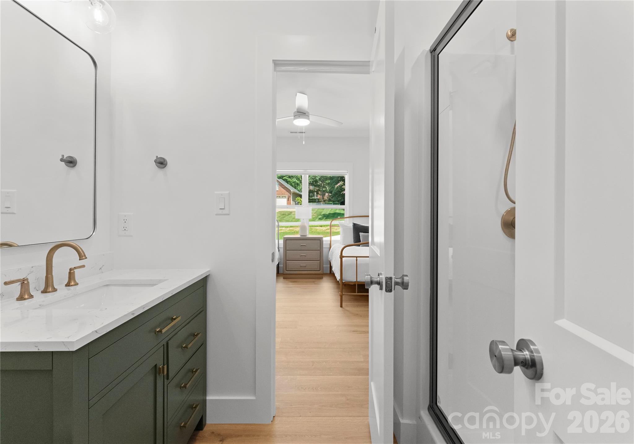 A sage-green vanity, stone-look countertop, and warm brass fixtures give this adjoining bath a polished feel. - 143 Hideaway Lane, Mooresville