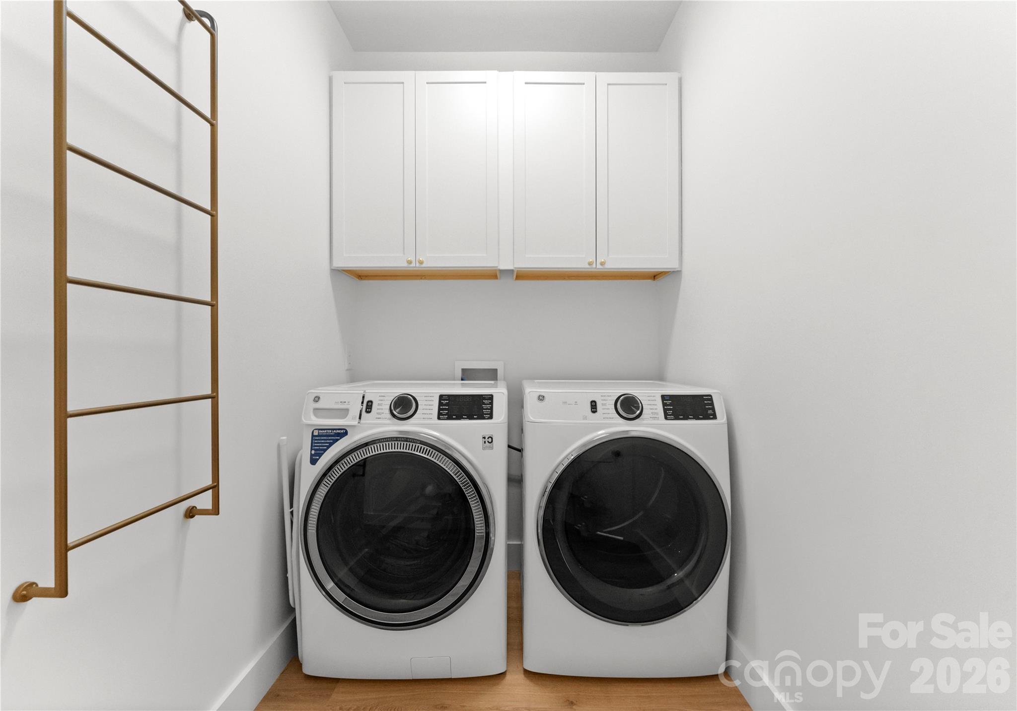The laundry room pairs a side-by-side washer and dryer with overhead cabinetry for convenient storage. - 143 Hideaway Lane, Mooresville