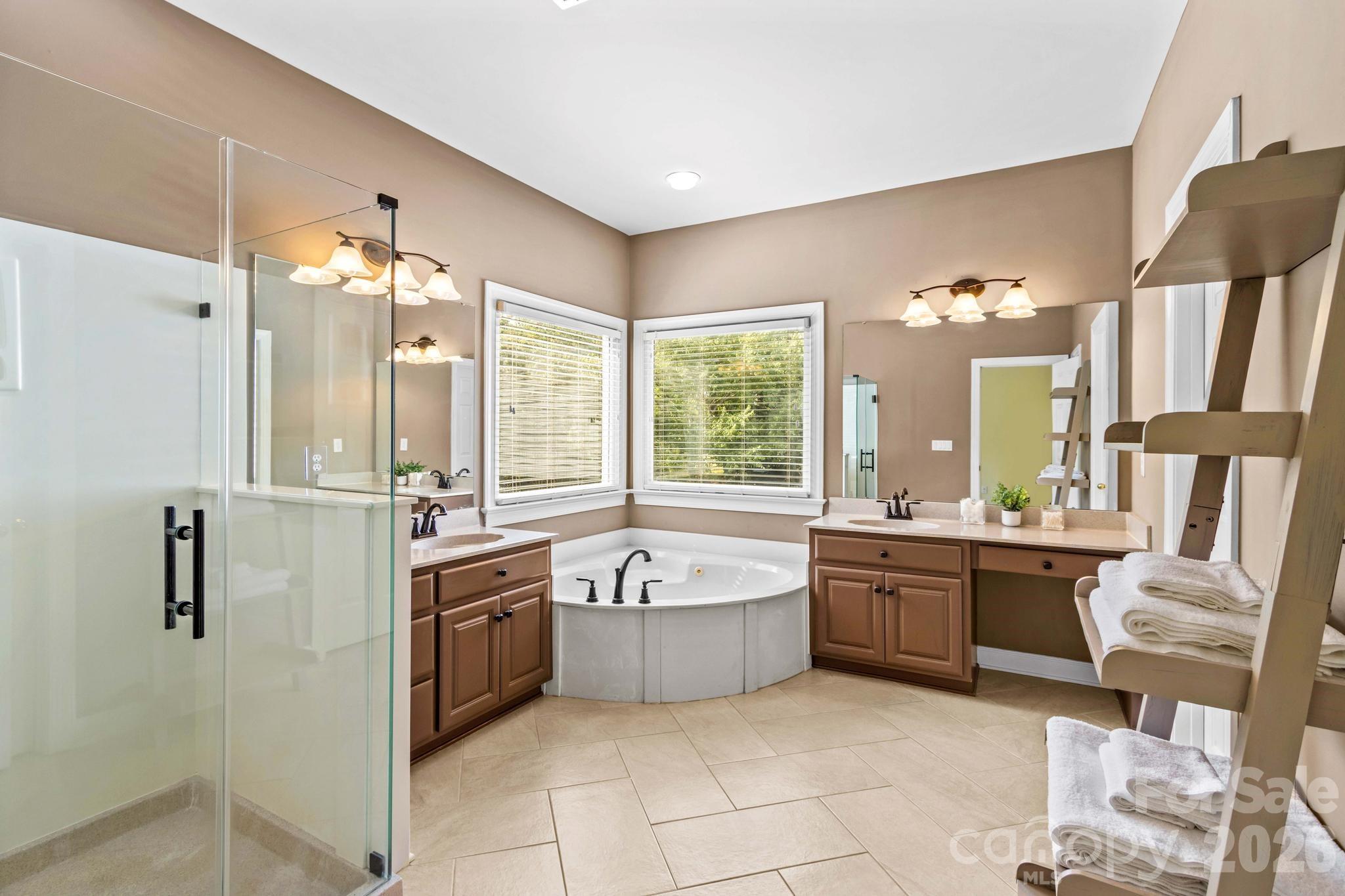 Primary bathroom has dual vanities, corner tub, frameless shower, and custom shelving in closet. - 12822 Cadgwith Cove Drive, Huntersville
