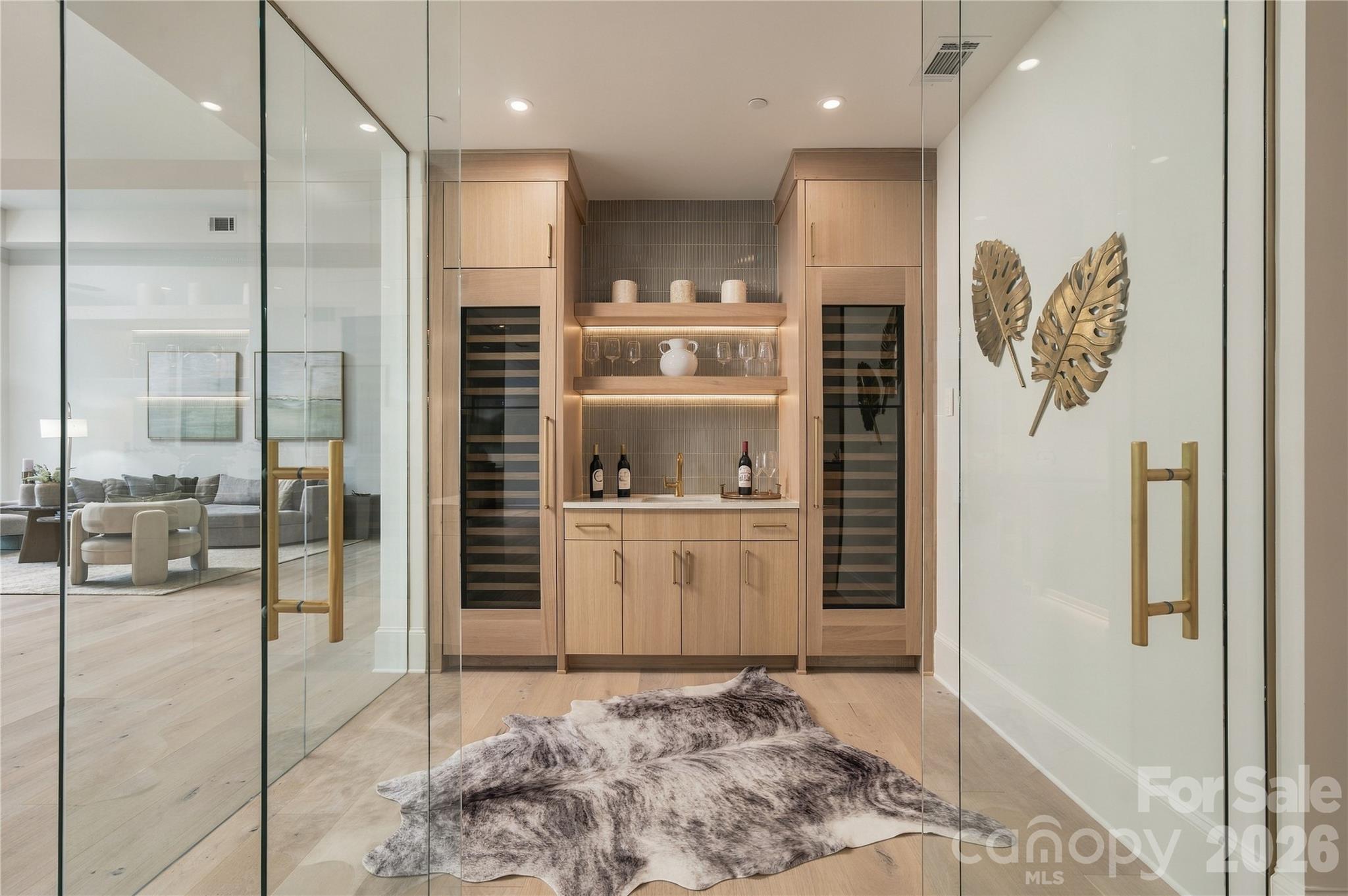 The striking wine room is beautifully finished with glass-enclosure, dual wine refrigerators, custom cabinetry, illuminated shelving and a wet bar for effortless entertaining. - 409 Queens Road, Charlotte