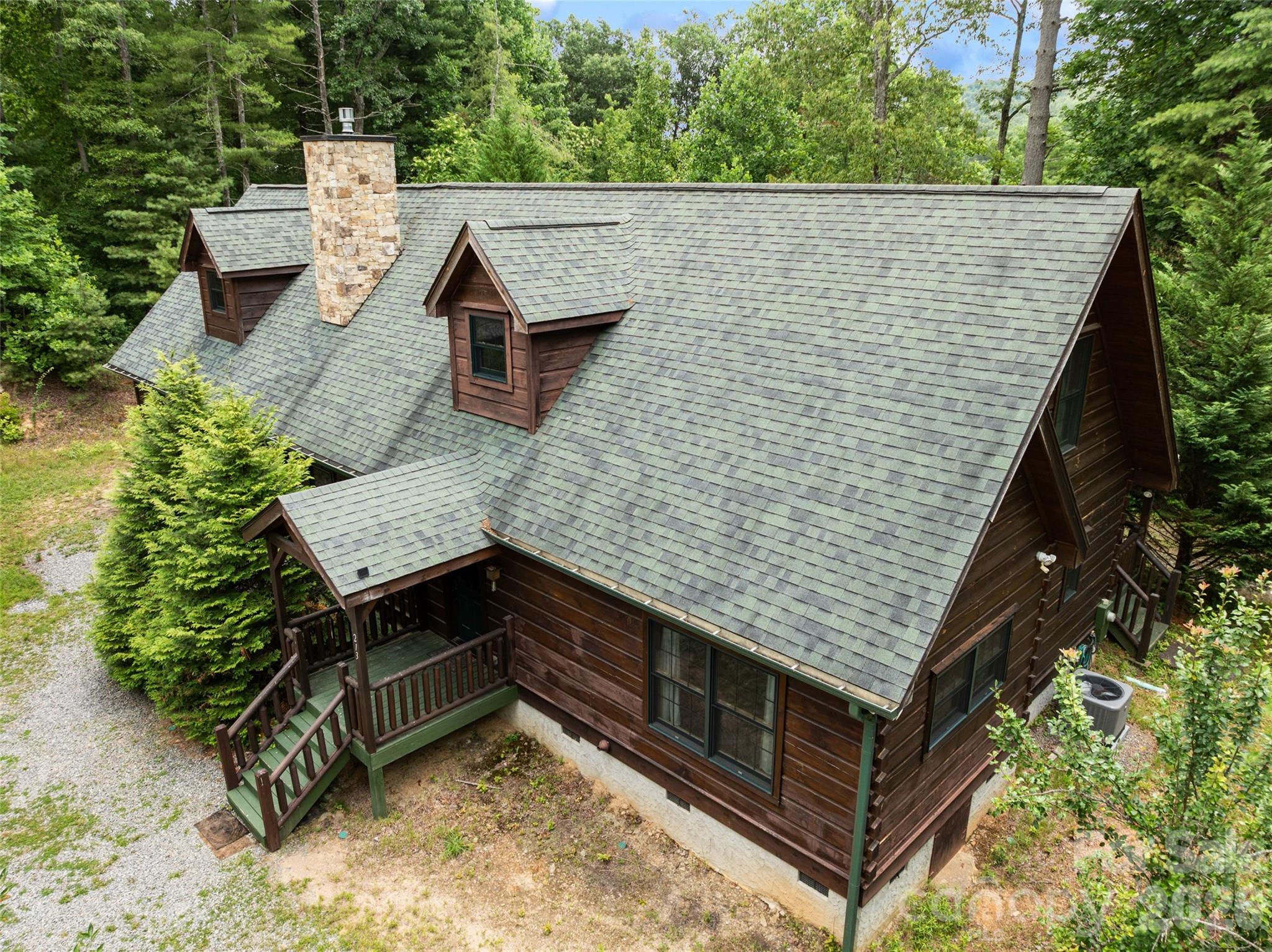 Get a bird's-eye view of your private mountain getaway. This sweeping drone shot highlights the home's impressive rustic architecture, showcasing the seamless blend of log-style accents, an inviting covered front porch, and a lush forest canopy right in your own backyard. - 213 Big Valley Road, Pisgah Forest