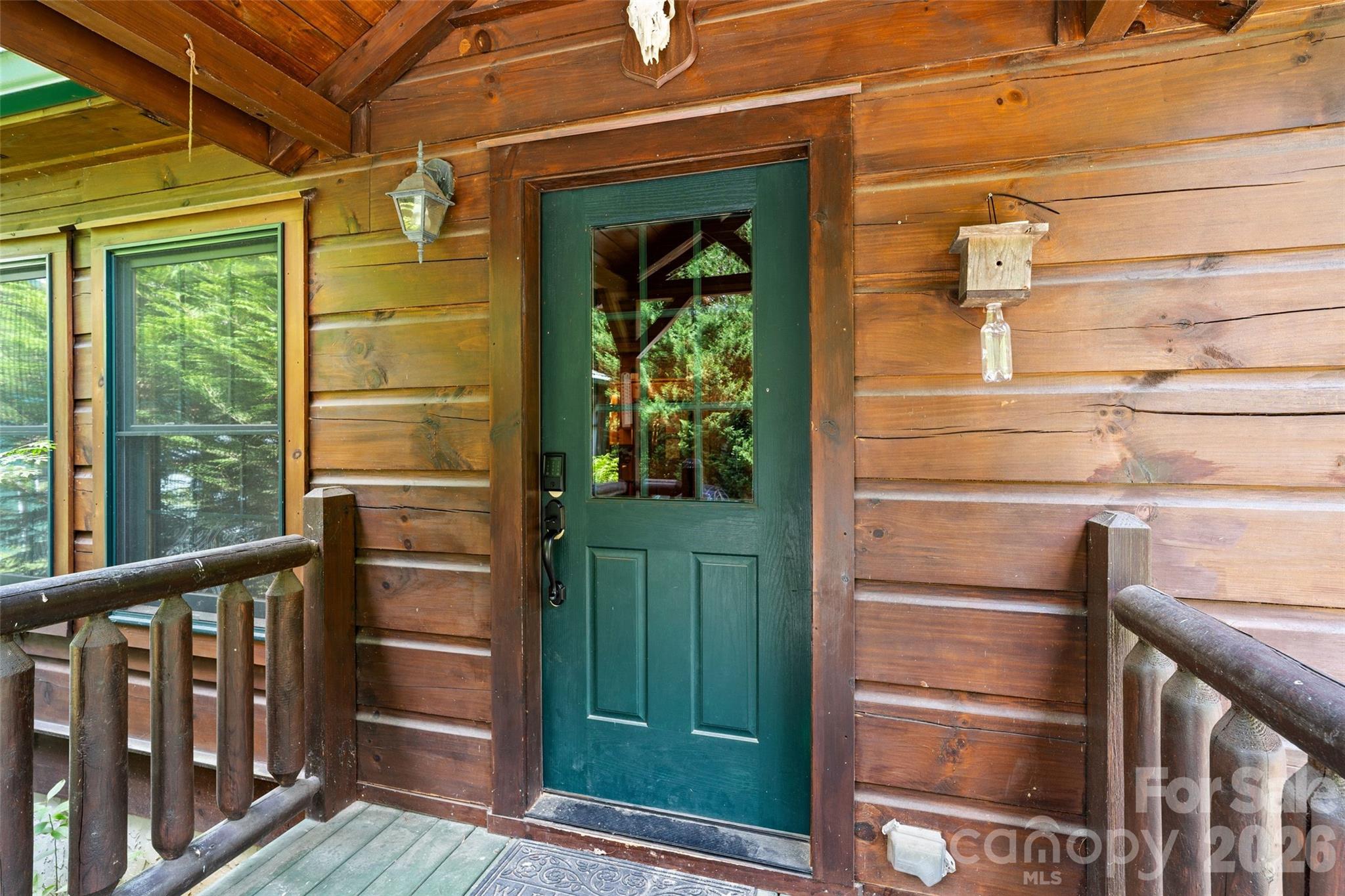 Welcome home through the charming back entrance. This private, covered rear porch features a beautiful green half-glass door that perfectly complements the rich log-style siding and warm wood-paneled ceiling. - 213 Big Valley Road, Pisgah Forest