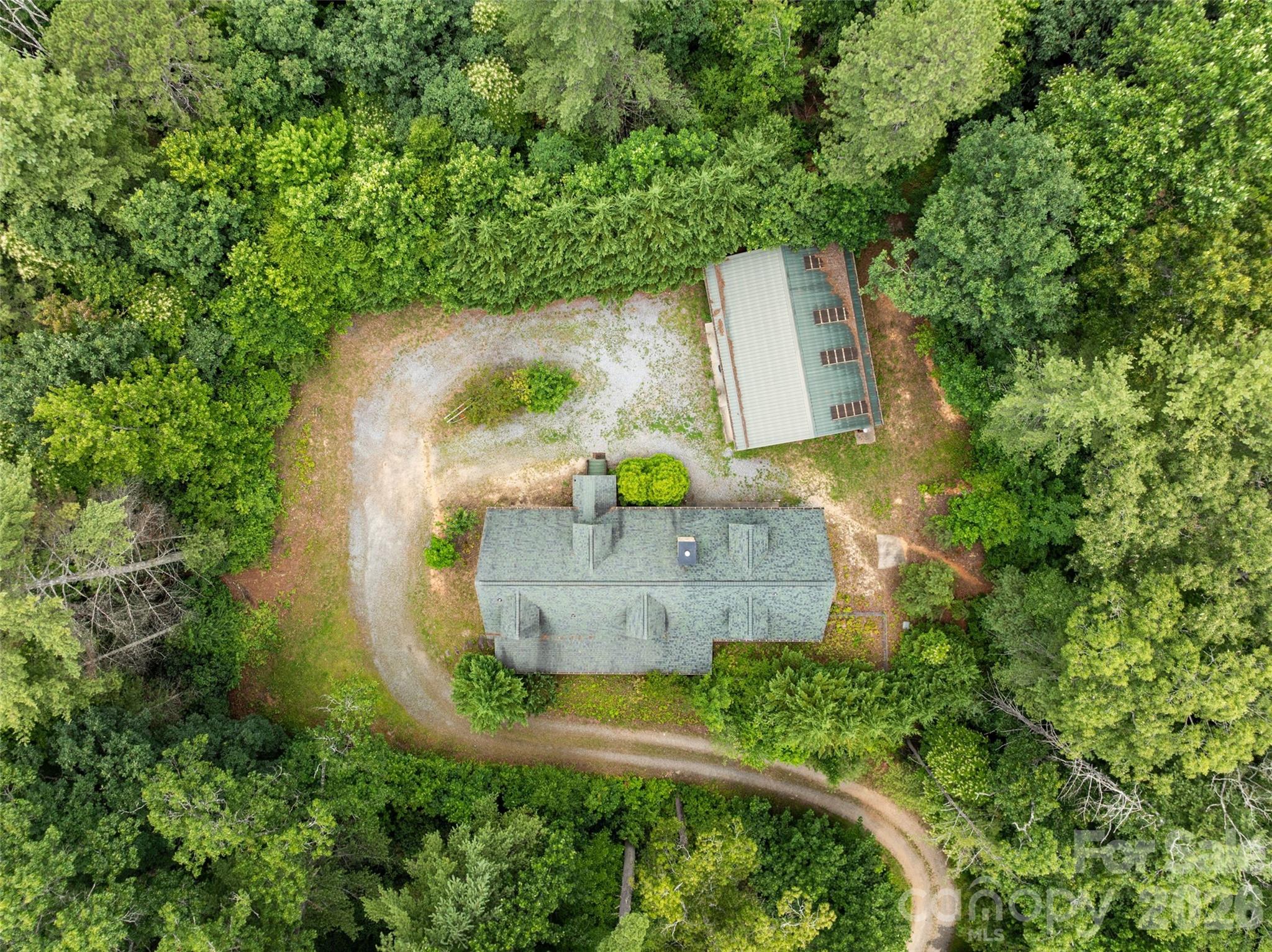 Experience ultimate privacy with this top-down aerial view revealing a true mountain compound. Enveloped by a dense canopy of mature trees, this secluded clearing perfectly accommodates the main residence, the massive detached shop, and a winding gravel drive with plenty of space to turn around and park. - 213 Big Valley Road, Pisgah Forest