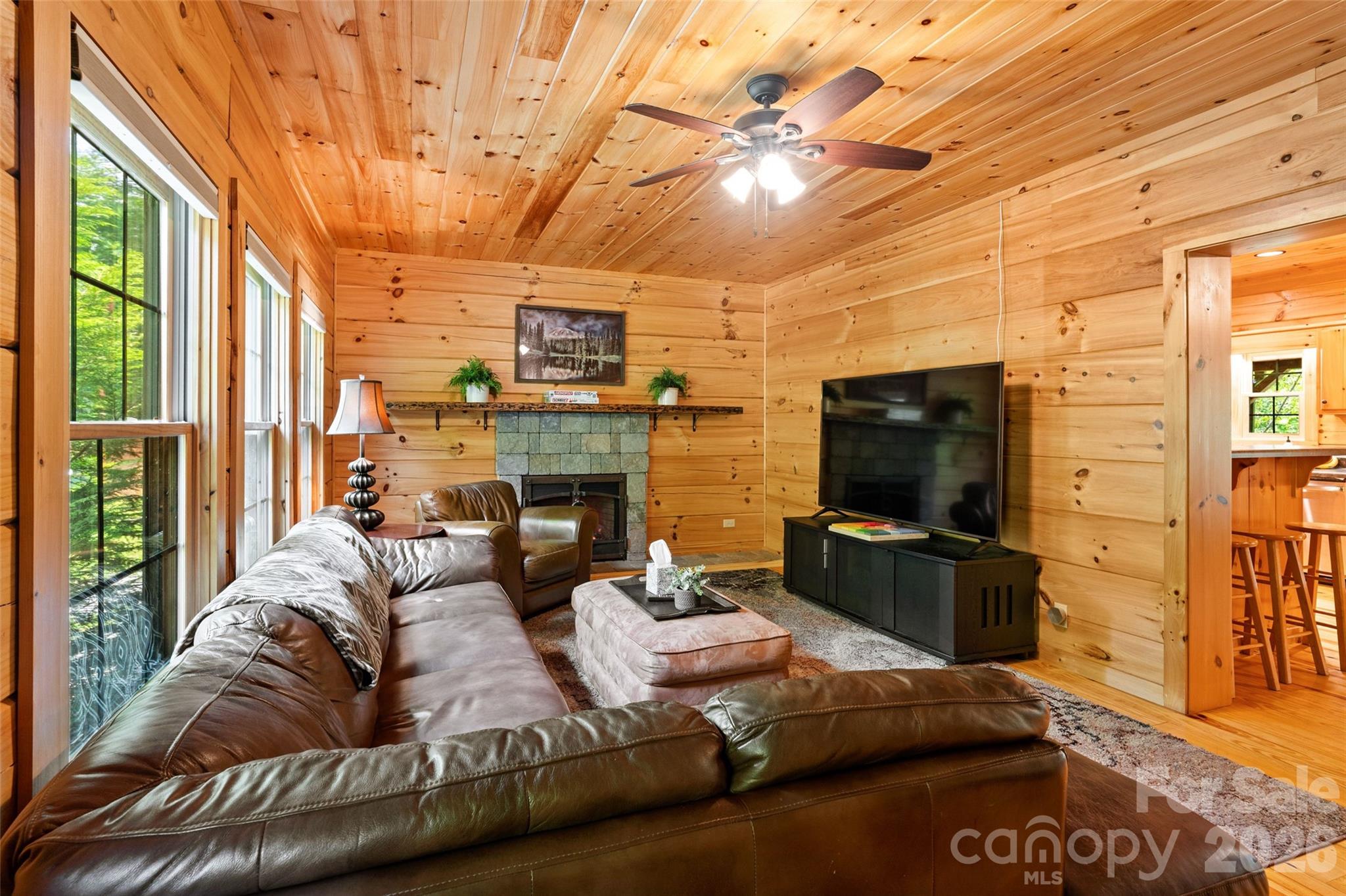This cozy main living space is the true heart of the home, perfectly blending rustic charm with everyday comfort. The stunning all-wood interior and hardwood floors are beautifully accented by the central fireplace and offer a seamless, open flow right into the adjacent kitchen area. - 213 Big Valley Road, Pisgah Forest