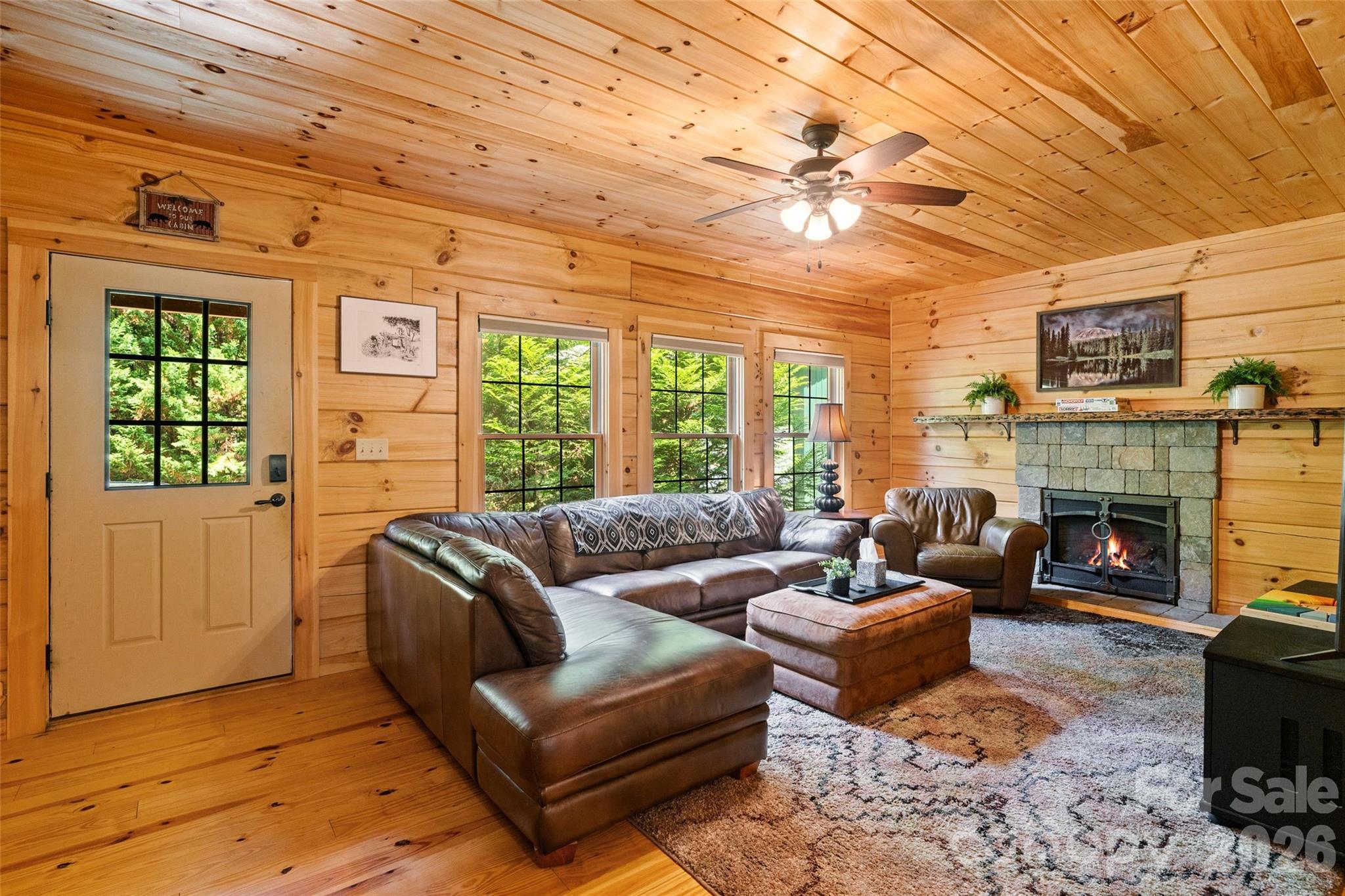 Build lasting memories in a living room designed for connection. The warm glow of the wood-paneled walls and the roaring stone fireplace create an unbeatable backdrop for holiday gatherings, quiet winter evenings, or lively family game nights after a day out on the trails - 213 Big Valley Road, Pisgah Forest