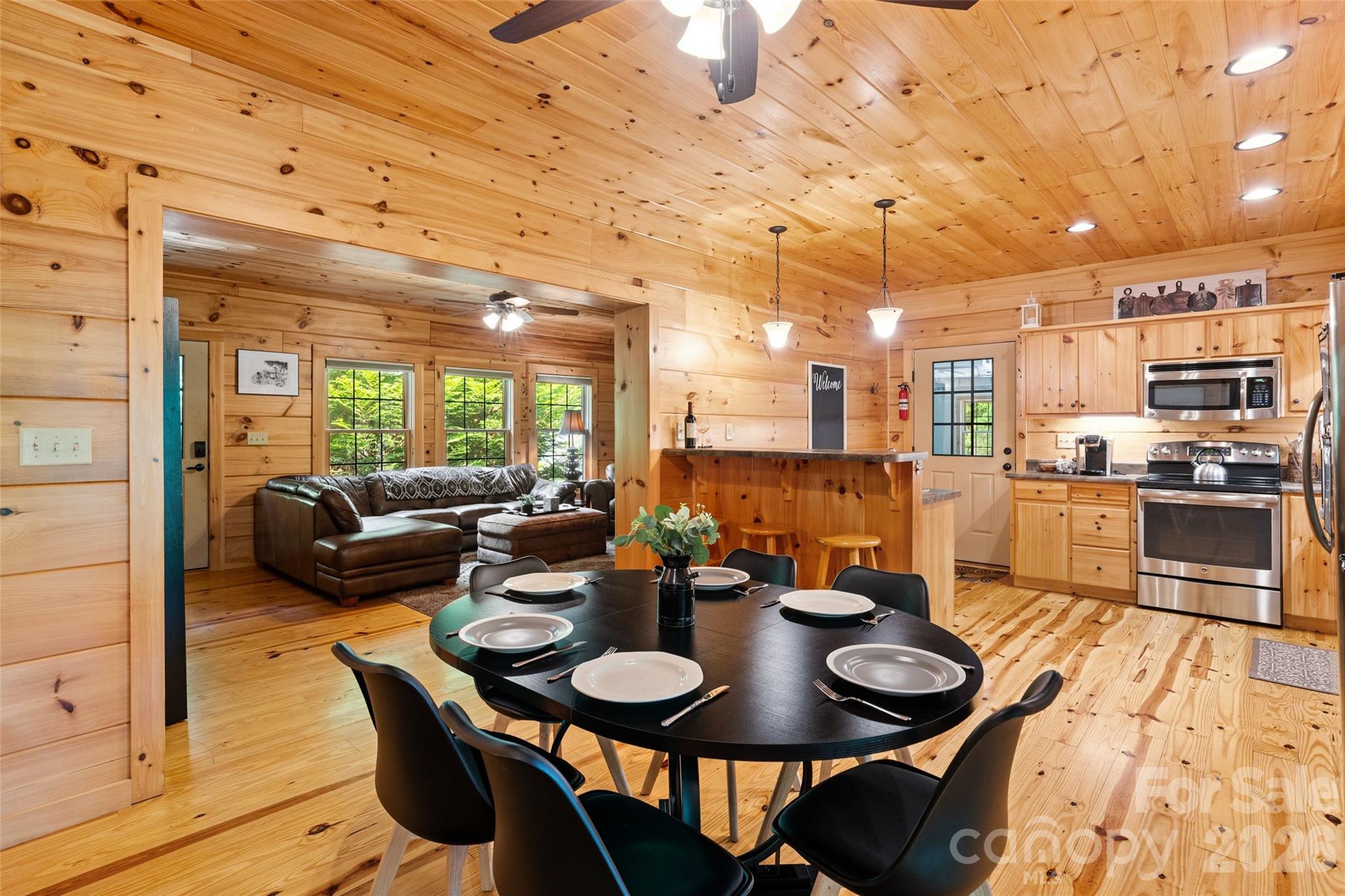 Gather round the table in this beautiful, all-wood dining space. The seamless transition between the living area, dining room, and kitchen creates a spacious, unified feel, beautifully tied together by continuous hardwood floors and warm knotty pine ceilings. - 213 Big Valley Road, Pisgah Forest
