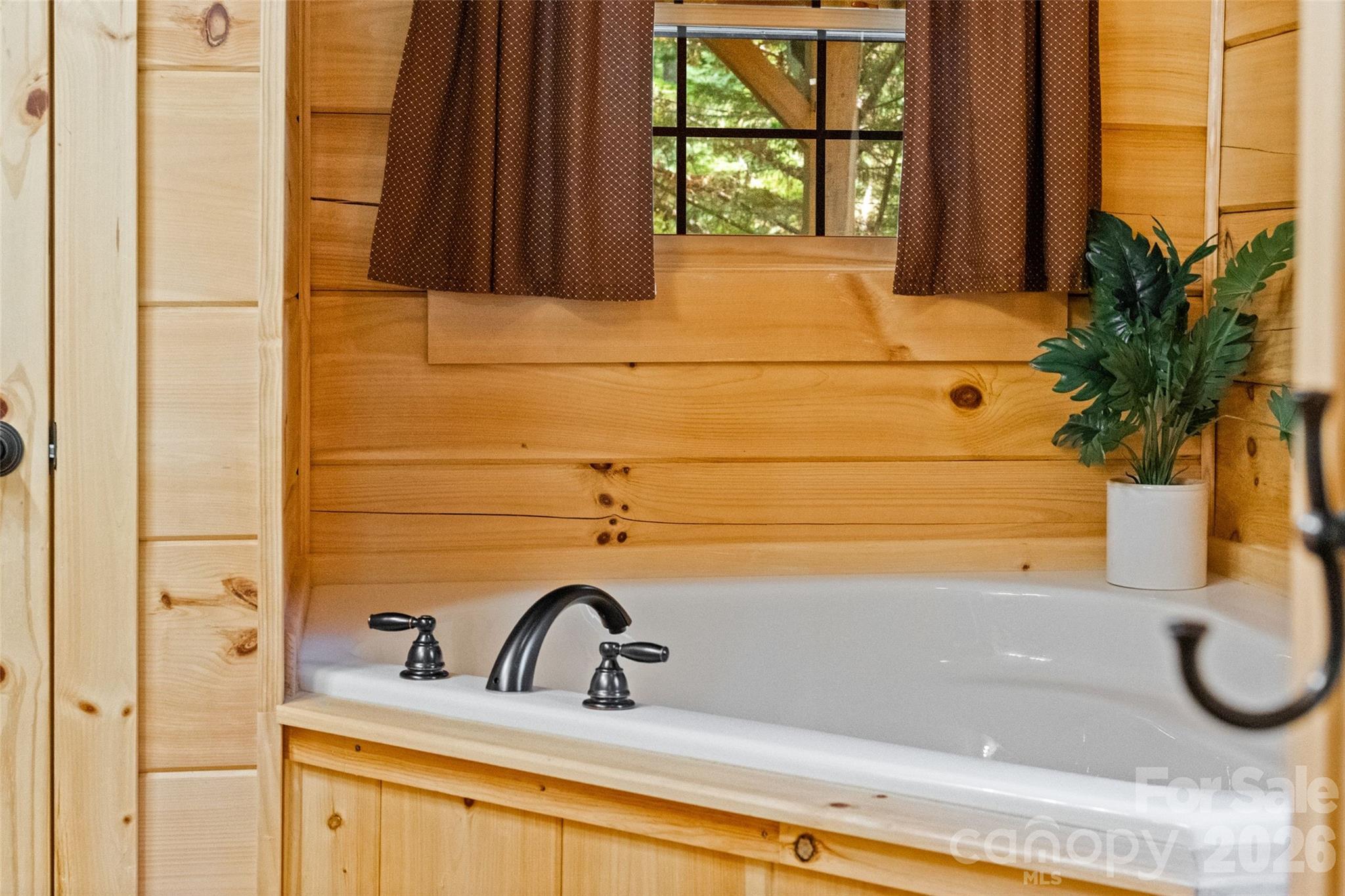 Relaxing primary ensuite garden tub highlighted by rustic tongue-and-groove wood walling, oil-rubbed bronze/dark hardware, and natural light. - 213 Big Valley Road, Pisgah Forest