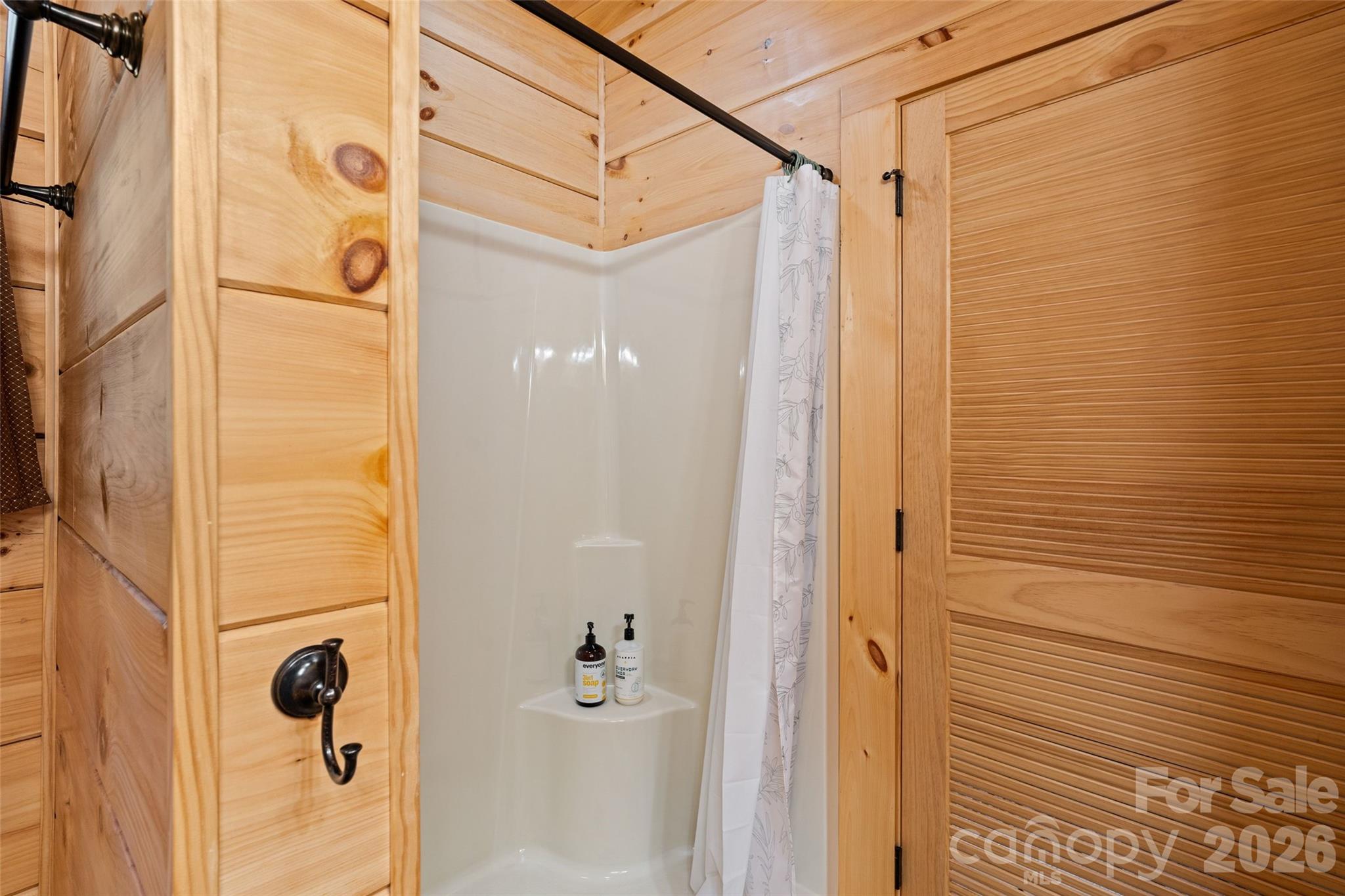 Clean and convenient walk-in shower stall in the primary bathroom, framed by beautiful natural pine wood construction and rustic oil-rubbed bronze hardware. - 213 Big Valley Road, Pisgah Forest