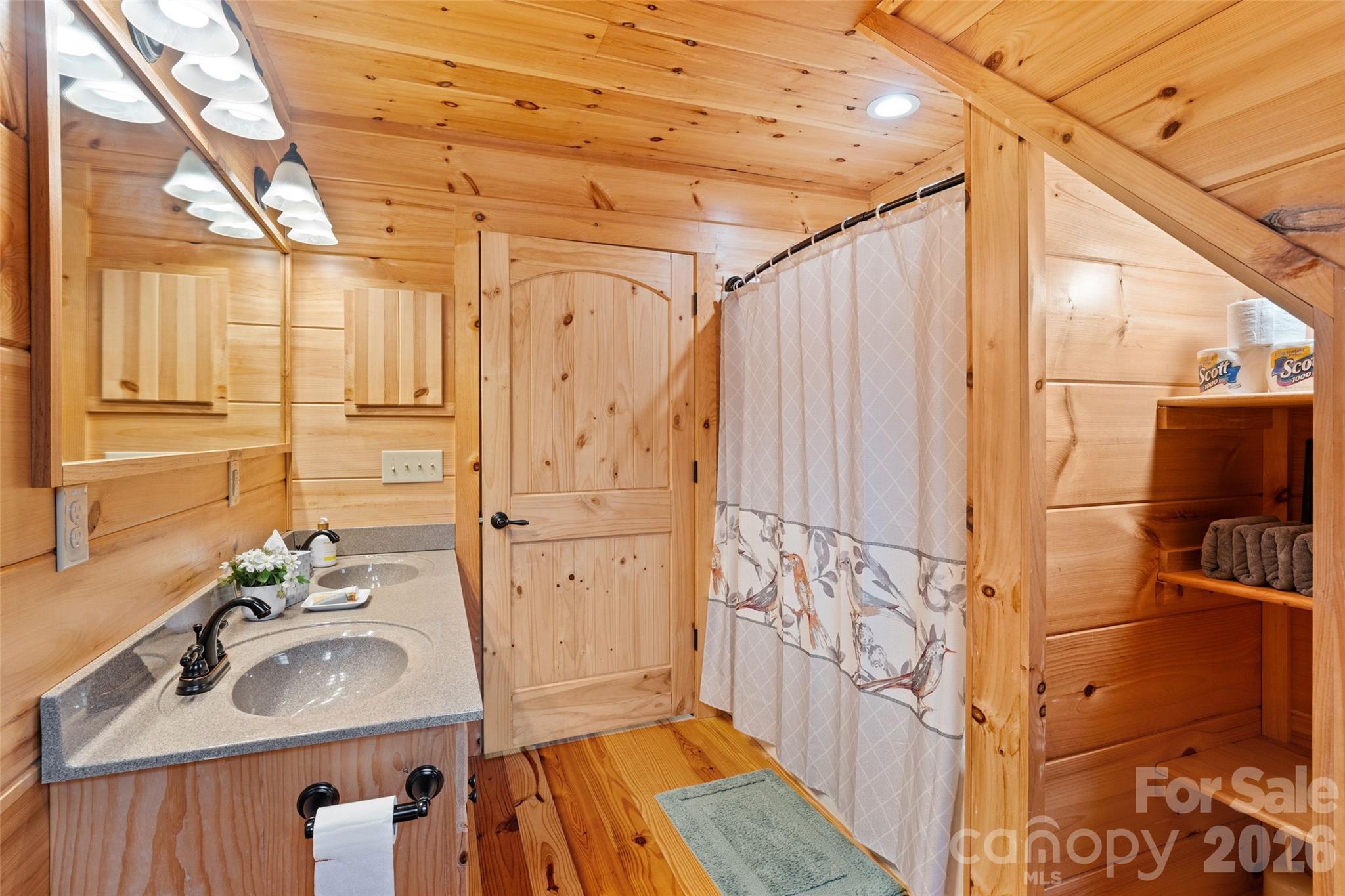 One of two full bathrooms located on the upper level, offering great convenience and rustic charm. Fully wrapped in warm knotty pine, this bath features a long double-sink vanity for effortless morning routines and a classic shower/tub combination. - 213 Big Valley Road, Pisgah Forest